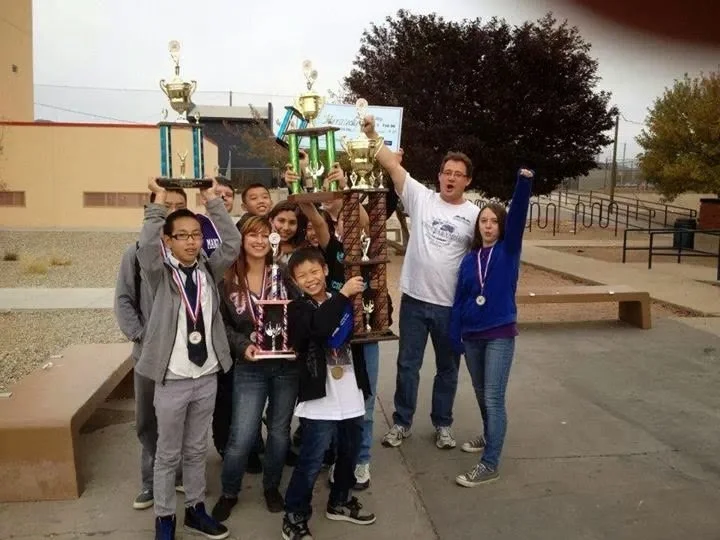 Group of children and a man celebrating with trophies and medals outdoors at school or park