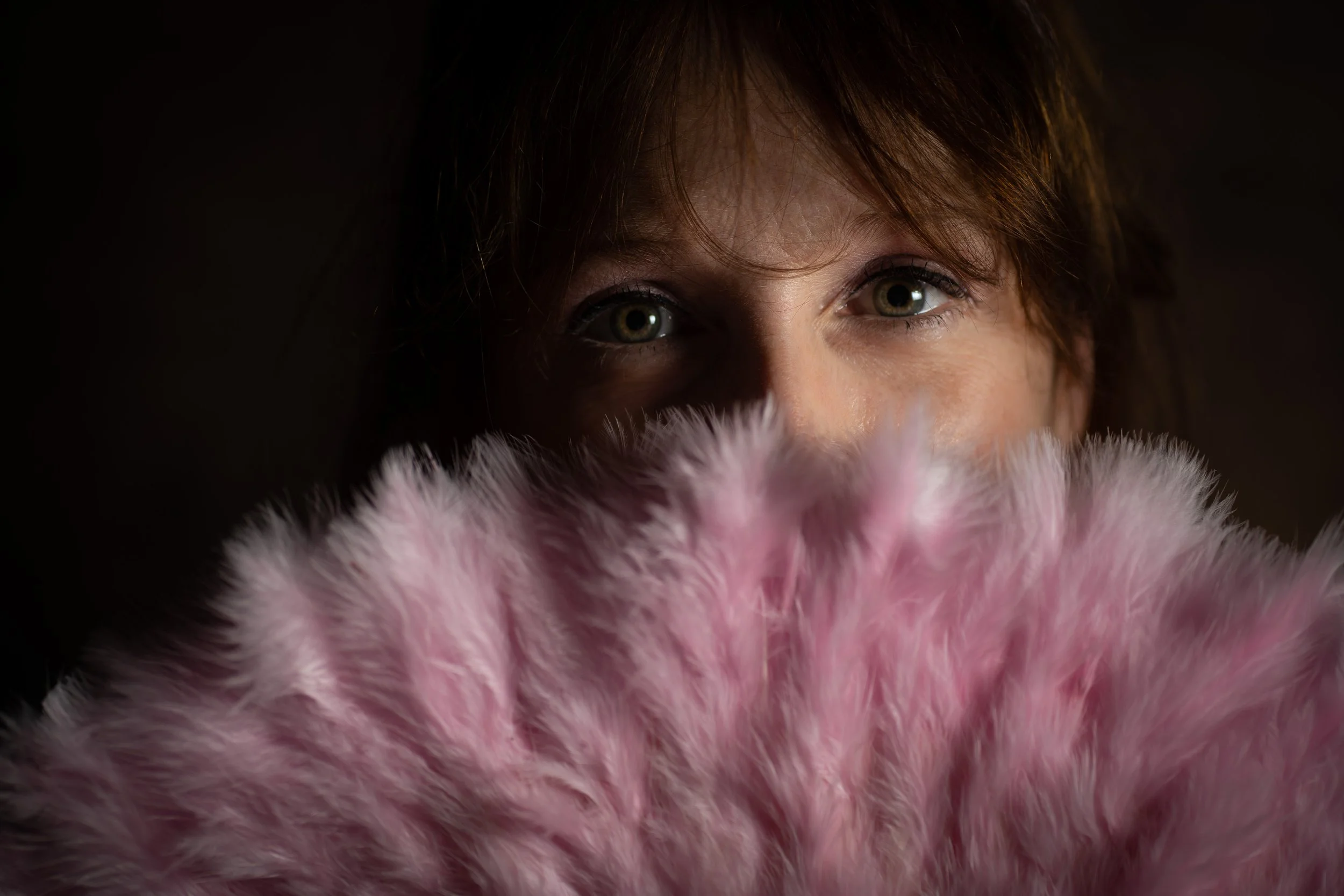 Zoom sur le visage d'une femme qui regarde vers le haut, partiellement cachée derrière une peluche ou un objet en peluche rose et blanc.