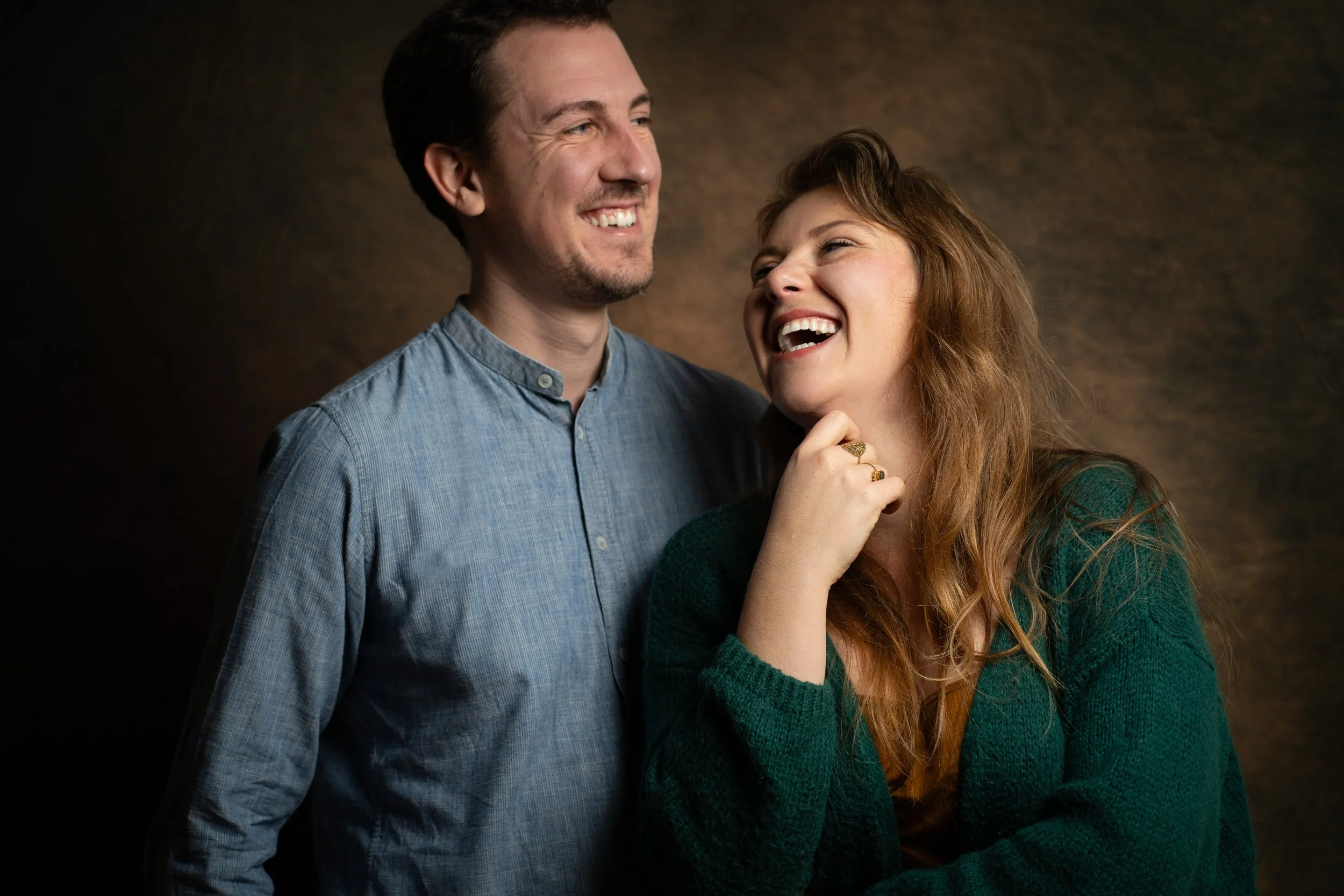 Un homme et une femme souriants, debout ensemble, en train de rire, contre un fond sombre.