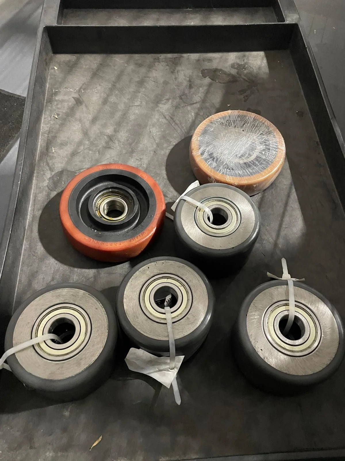 A metal cart holding five caster wheels, one wrapped and four with visible bearings, on a concrete floor.