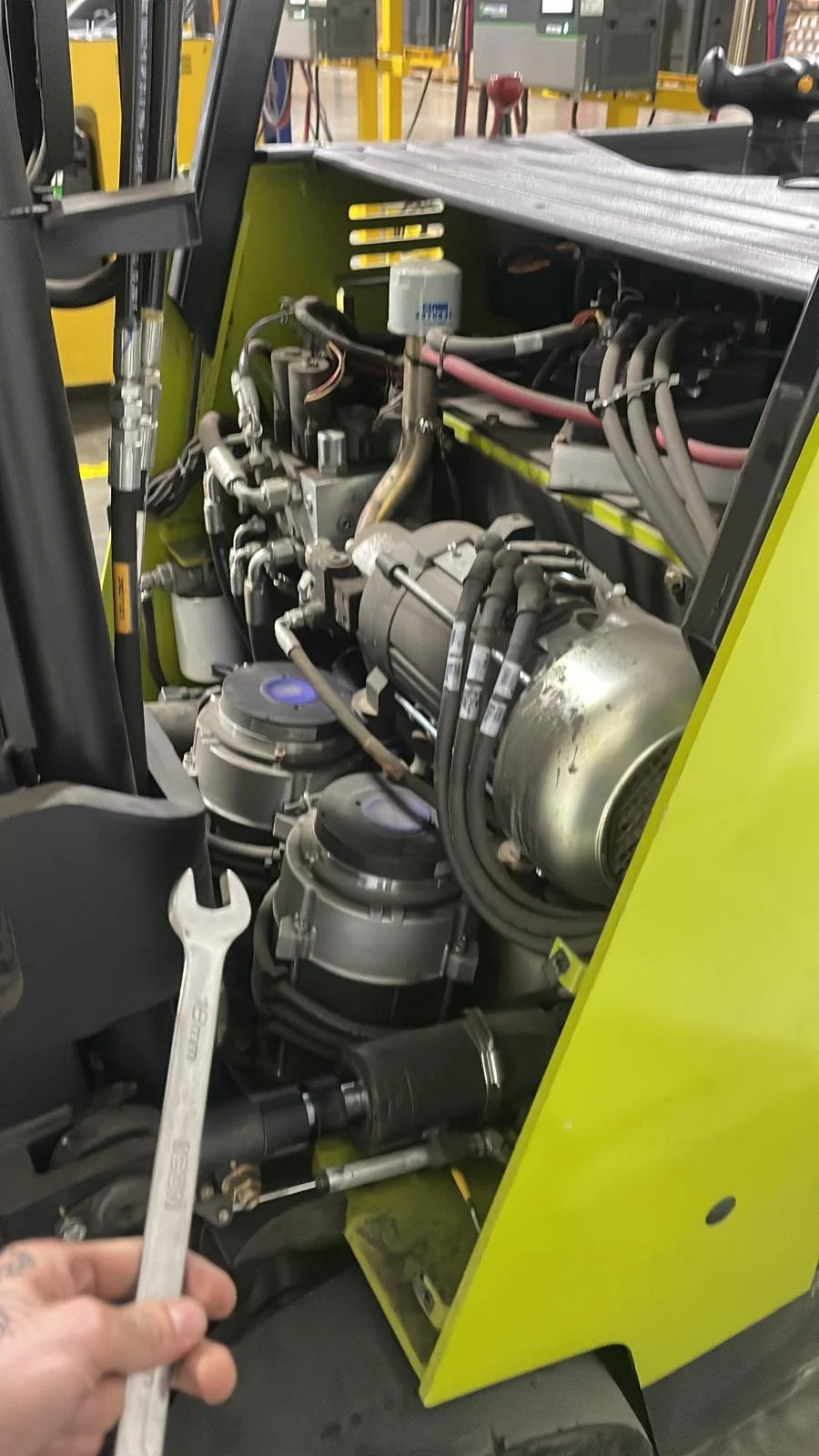 Close-up of the engine compartment of a forklift with a wrench held by a person.