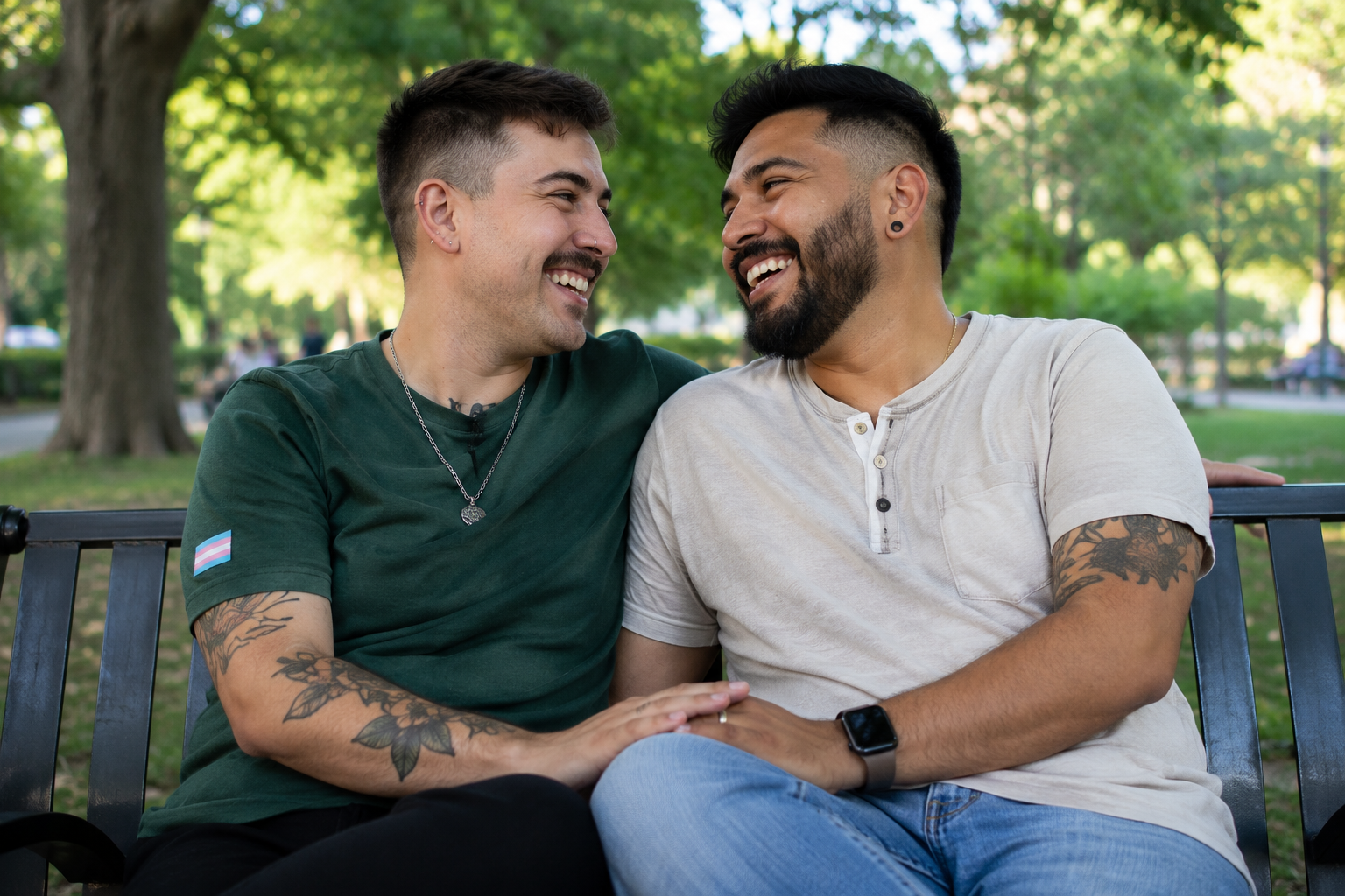 Two men sitting on a bench in a park, smiling and sharing an intimate moment. They are holding hands and looking at each other affectionately, with trees and greenery in the background.