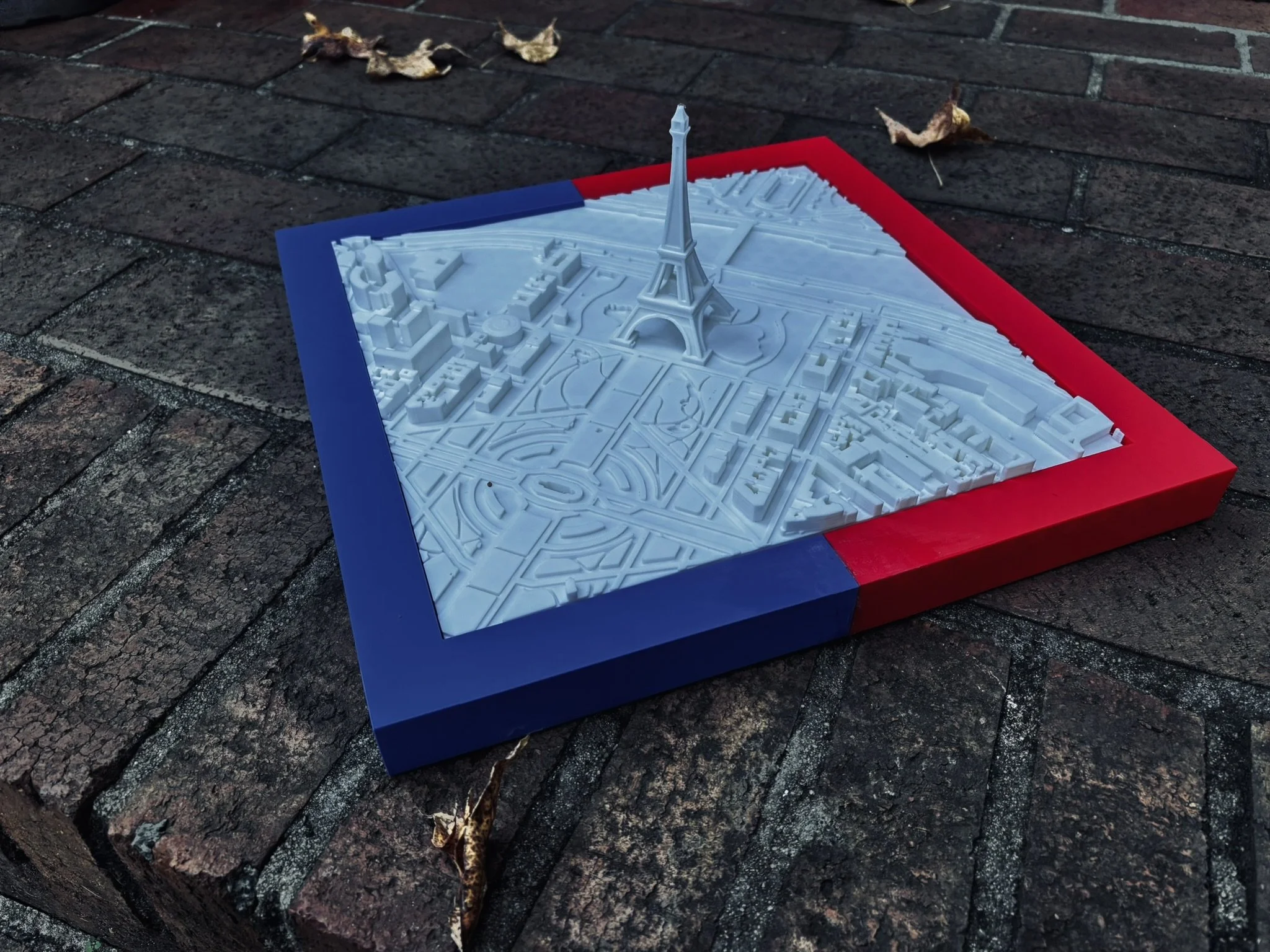 A detailed white architectural model of the Eiffel Tower and surrounding buildings on a blue and red base.