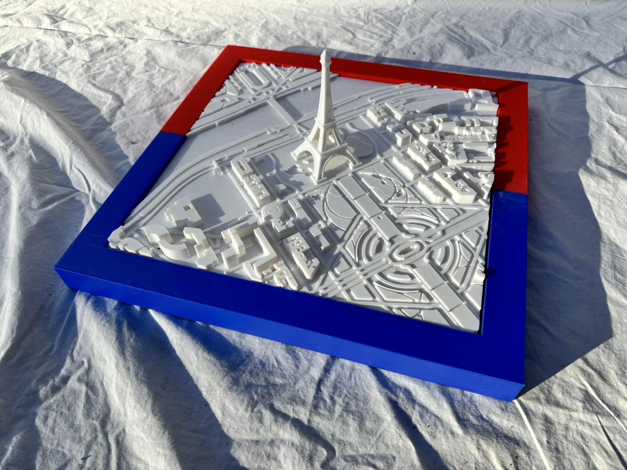 A white scale model of the Eiffel Tower on a map of Paris with a blue and red border.