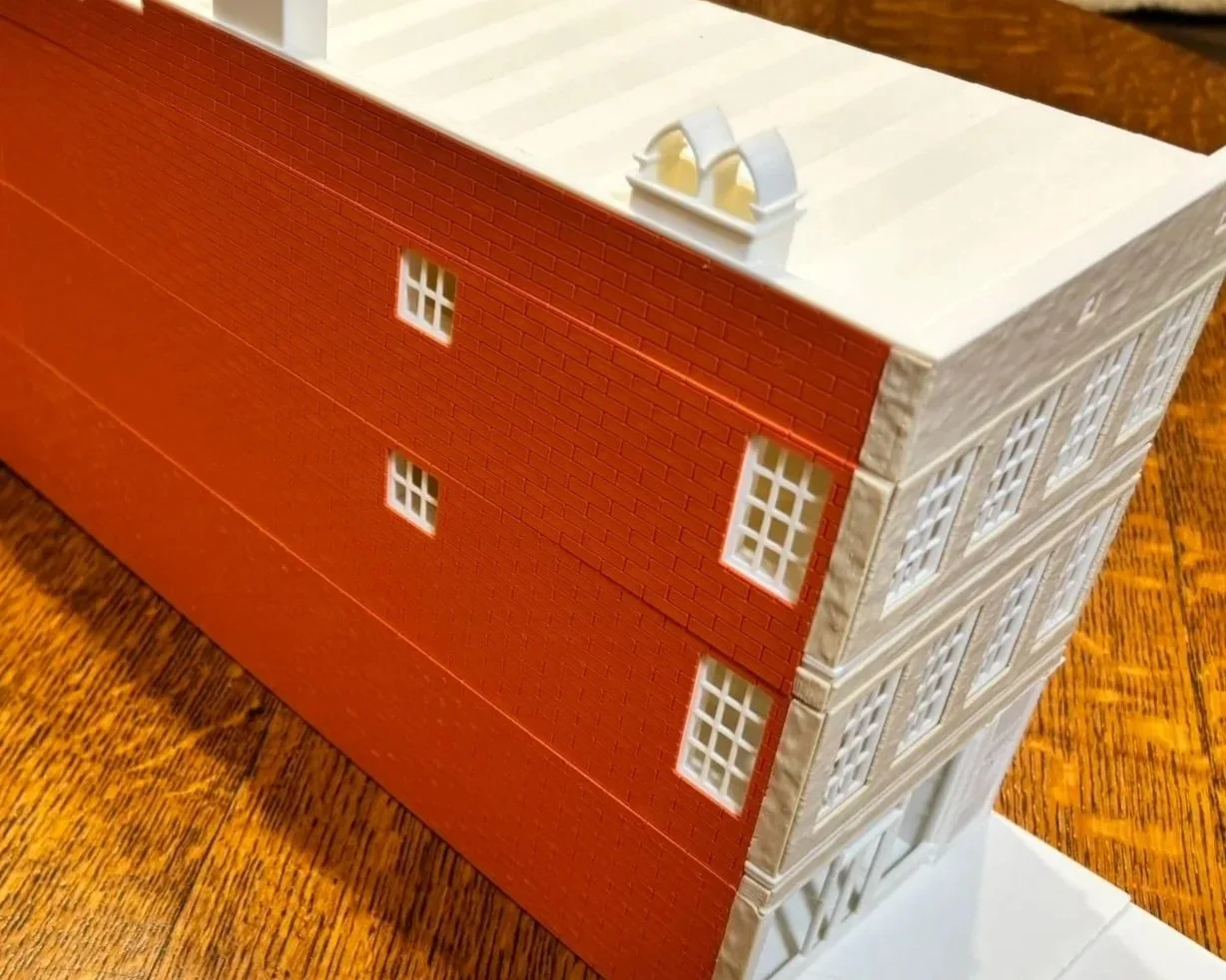 Model of a multi-story building with red and white walls, small windows, and a gray roof.