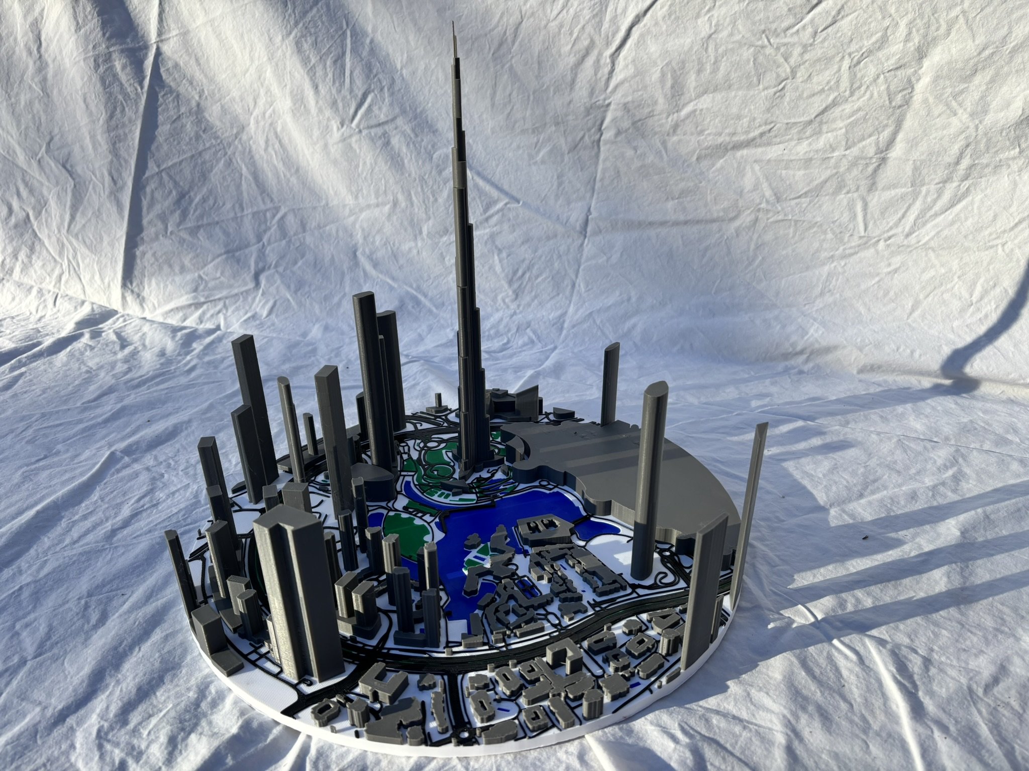 A 3D-printed model of a city or map with various black, gray, and green terrain features and structures.