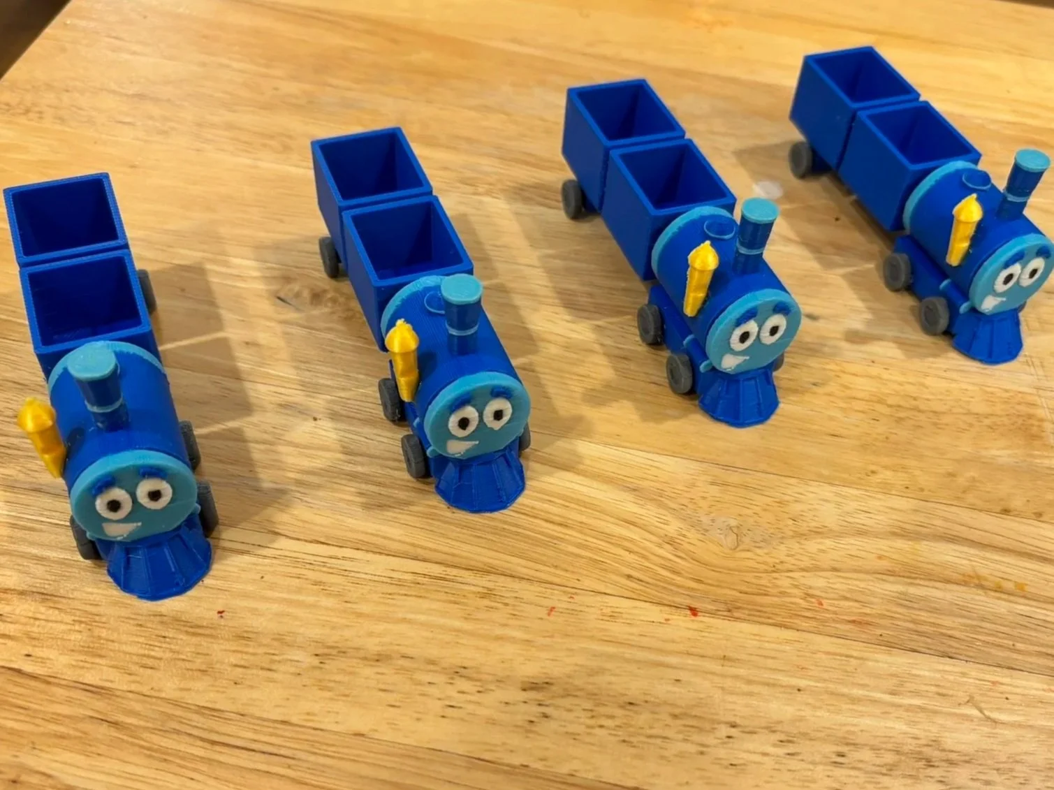 Four blue toy train cars with smiling faces on a wooden surface.