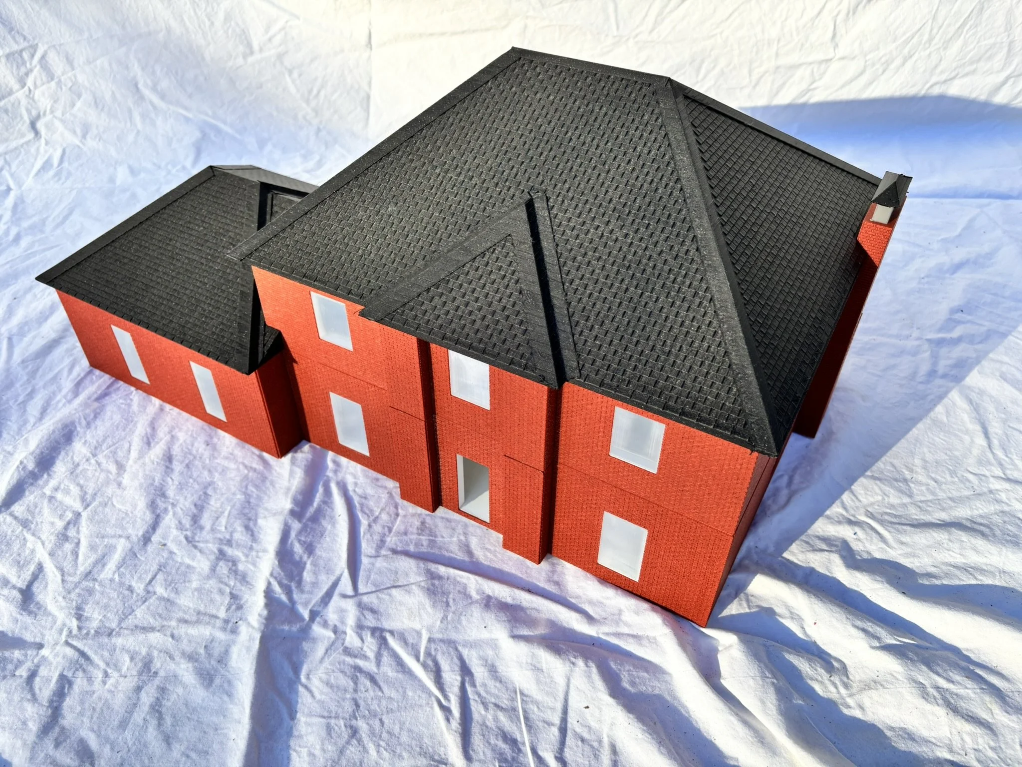 A model of a red brick house with a black shingle roof, white window frames, and a chimney.
