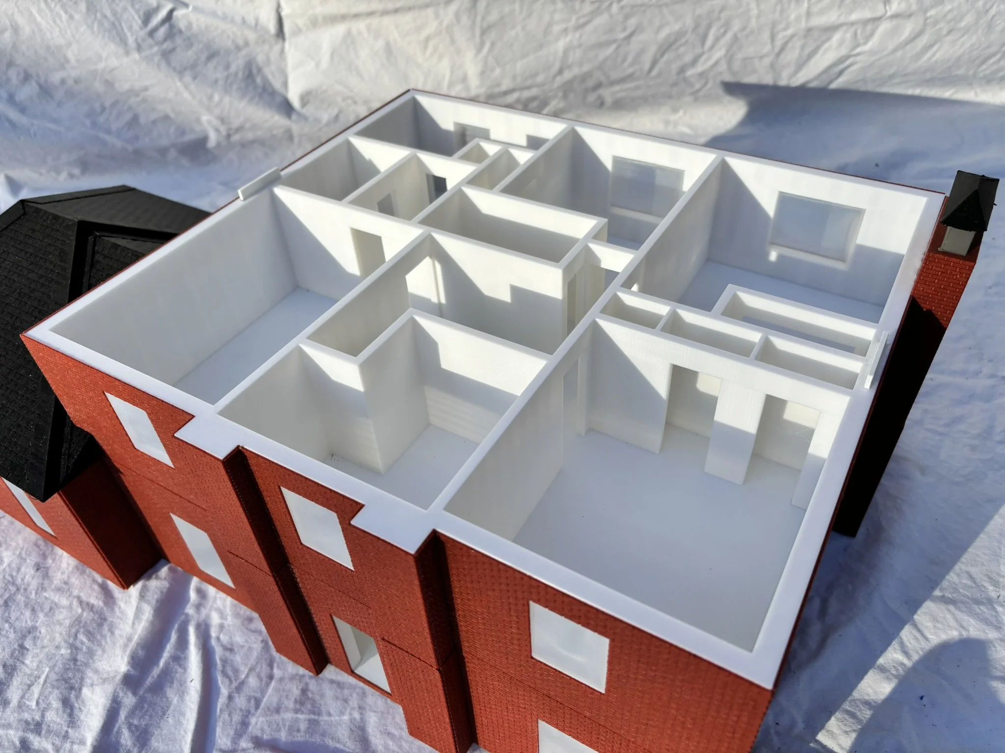 A white architectural model of a house with multiple rooms and windows, placed on a red base.