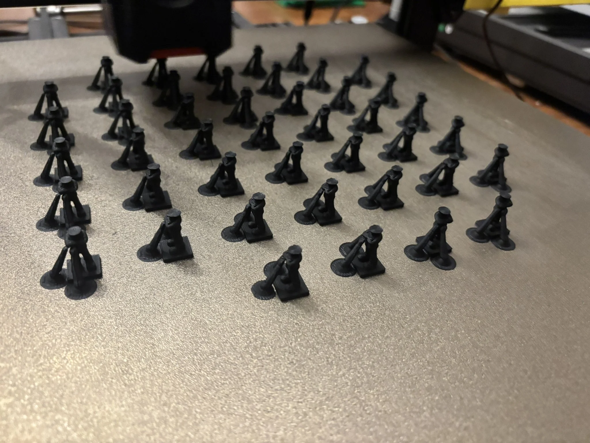 Close-up of multiple small black plastic parts with a tripod-like design, arranged on a gray surface. 