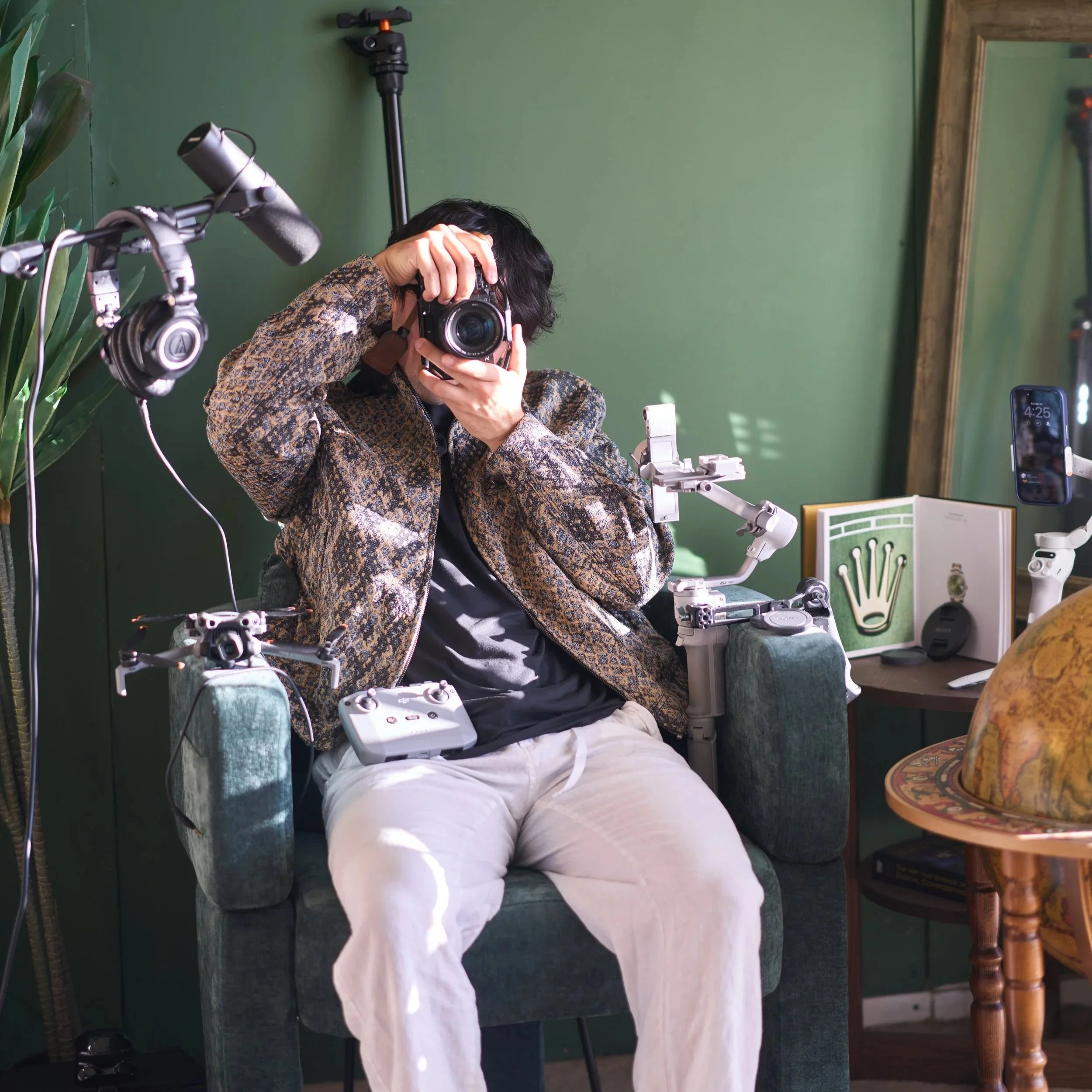 A photographer sitting on a green armchair taking a photograph with a camera, with photography equipment on the table. This amazing photo was captured and edited by Los Angeles-based Kairos VZN Premium Media Production.