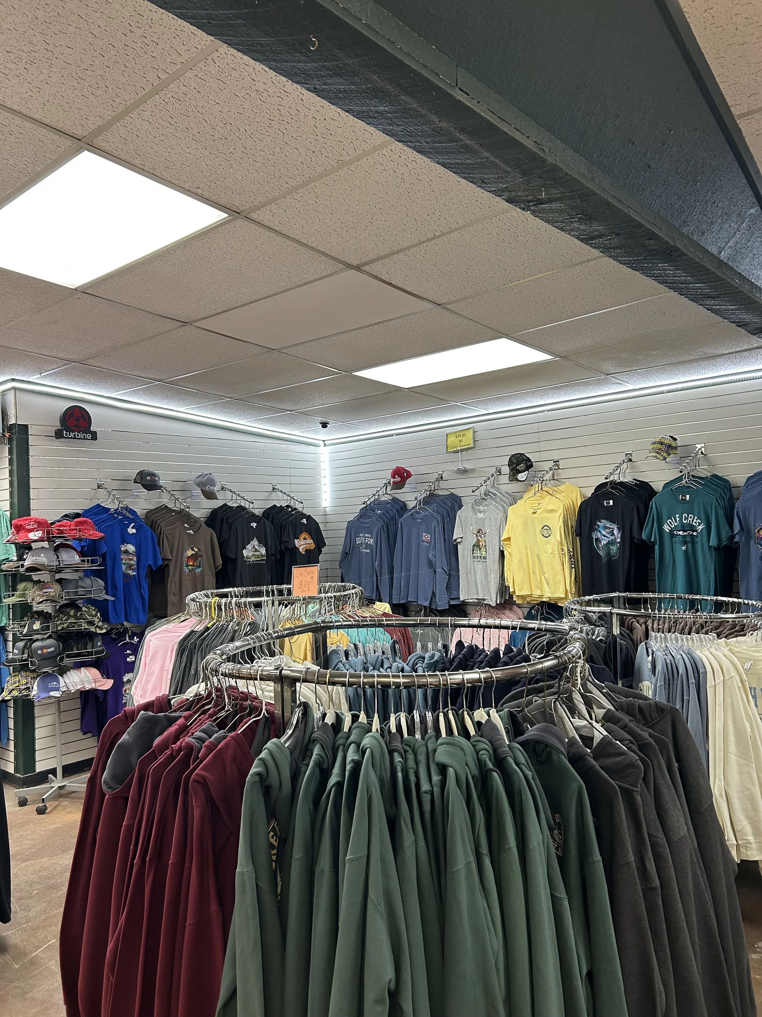 Clothing store display with racks of hoodies and hats under ceiling lights.