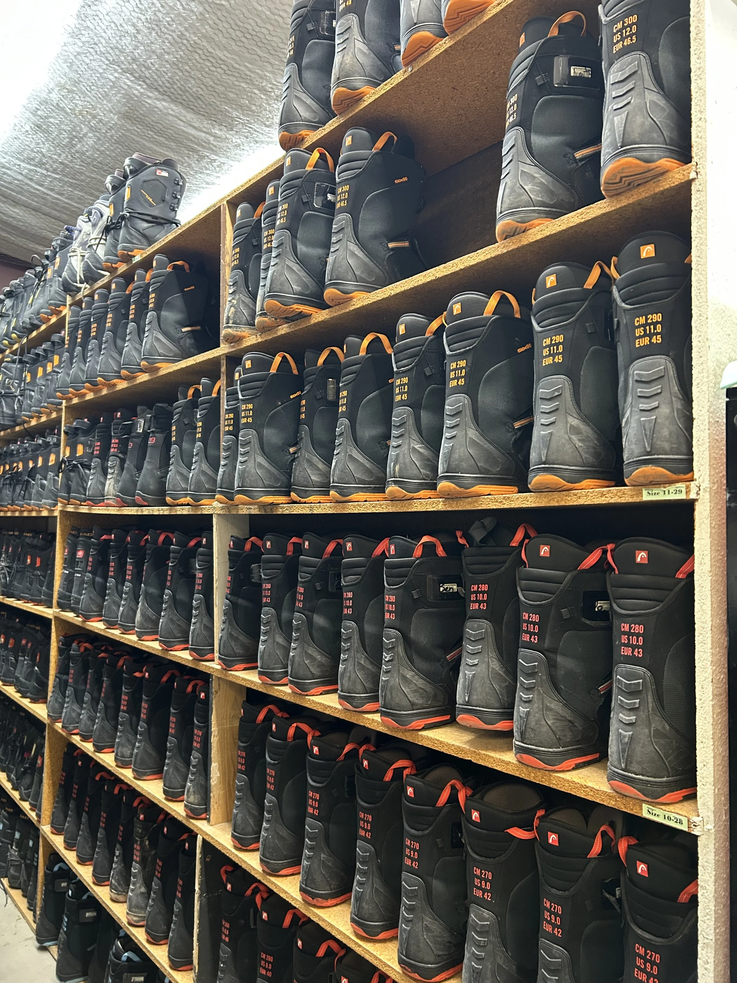 Shelves filled with waterproof boots, arranged by size and style, with some featuring orange accents and labels showing size conversions.