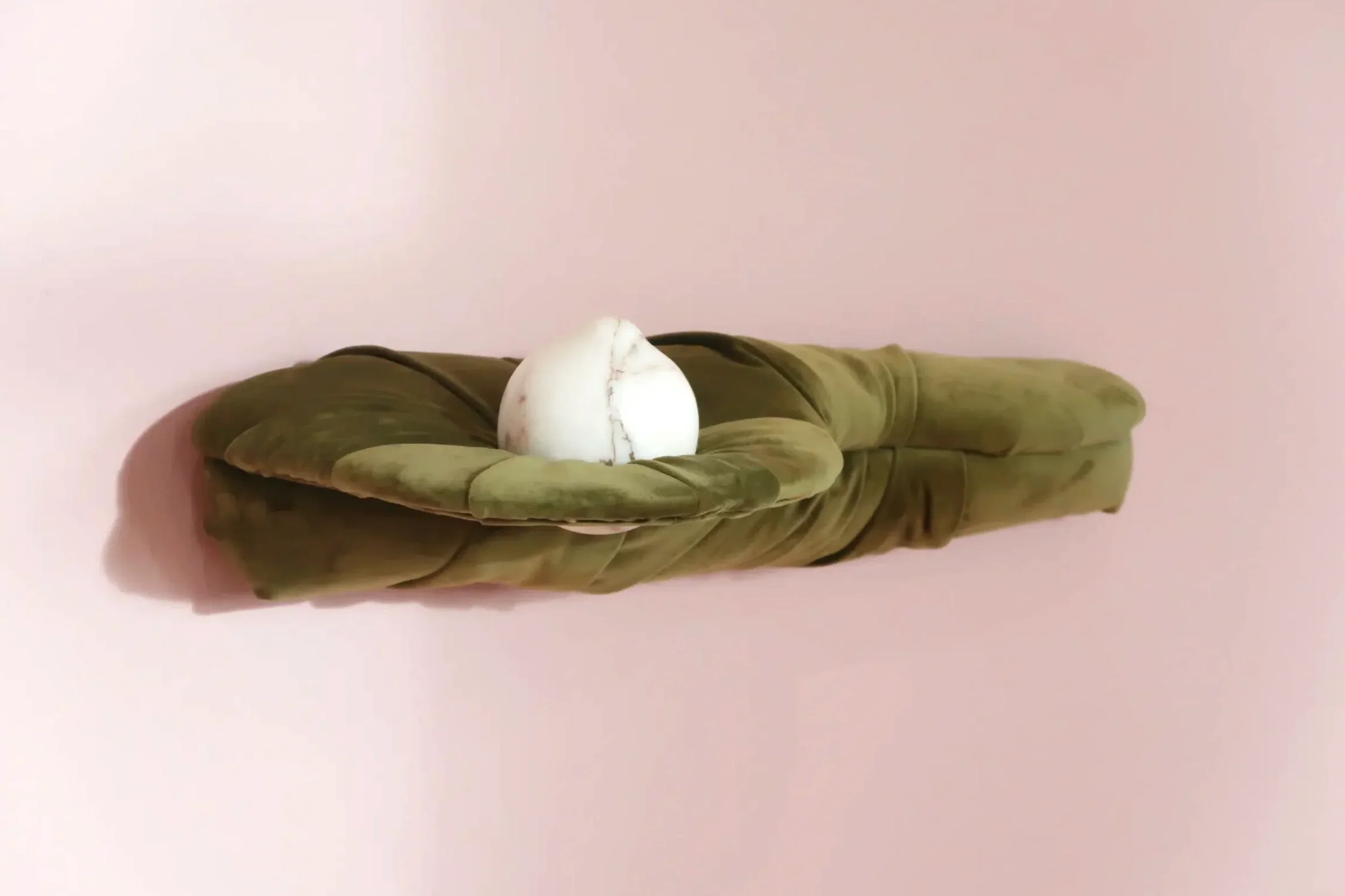 A white marble sculpture resting in a green velvet shelf against a light pink wall.