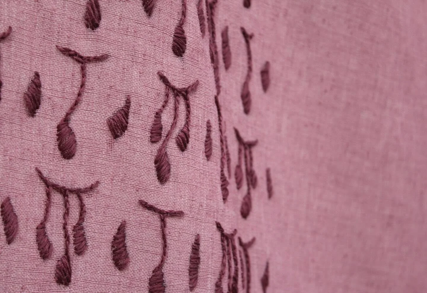 Close-up of pink fabric with embroidered brown teardrop shapes.