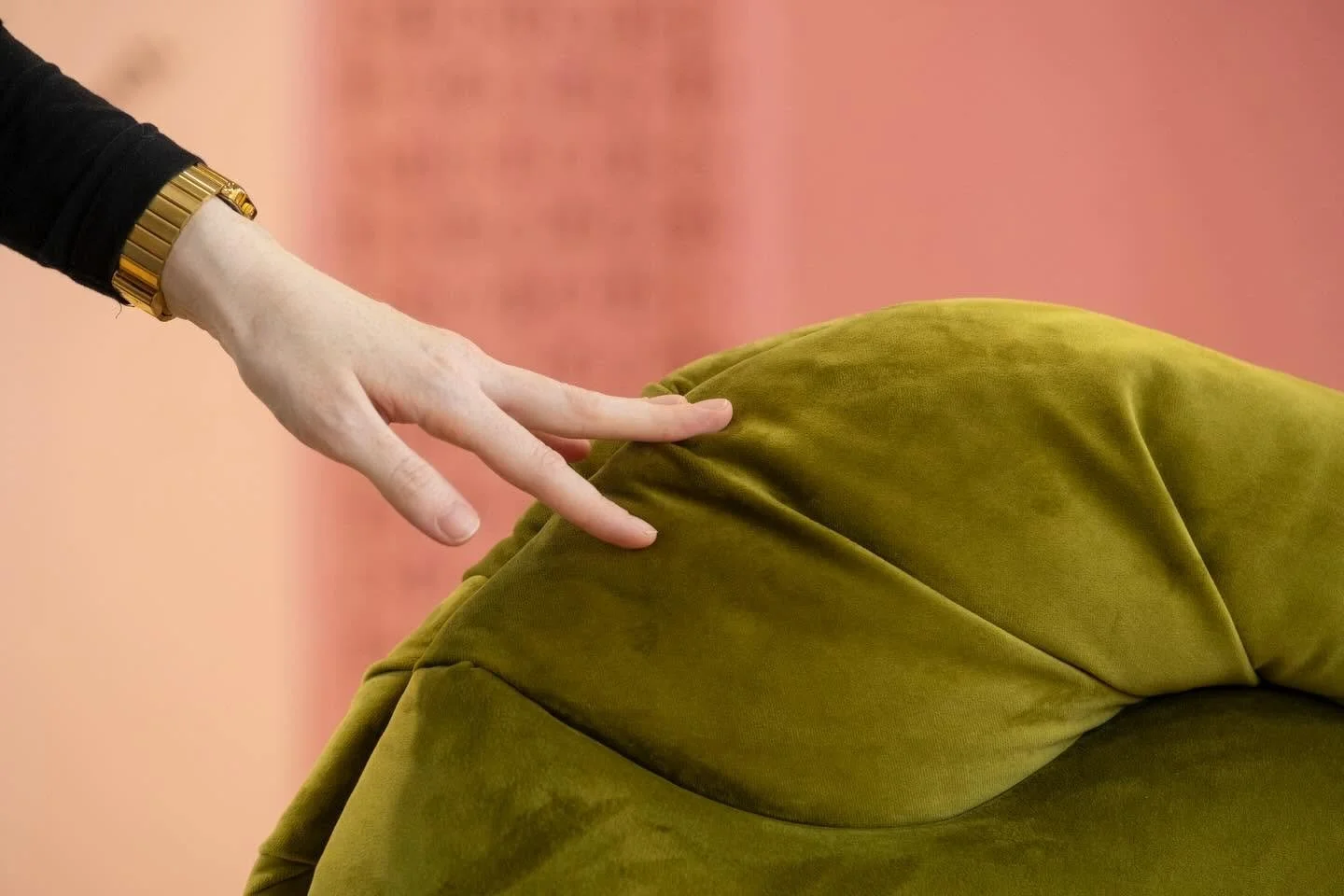 A person with a gold watch stretching their hand out to touch a green velvet sculpture.