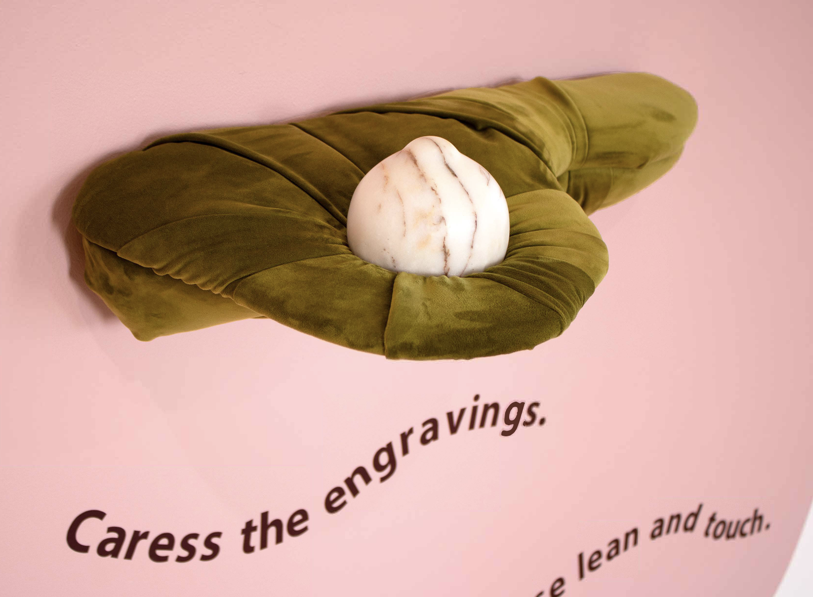 Green velvet shelf with a white marble sculpture placed on top, on pink background, with partially visible text.