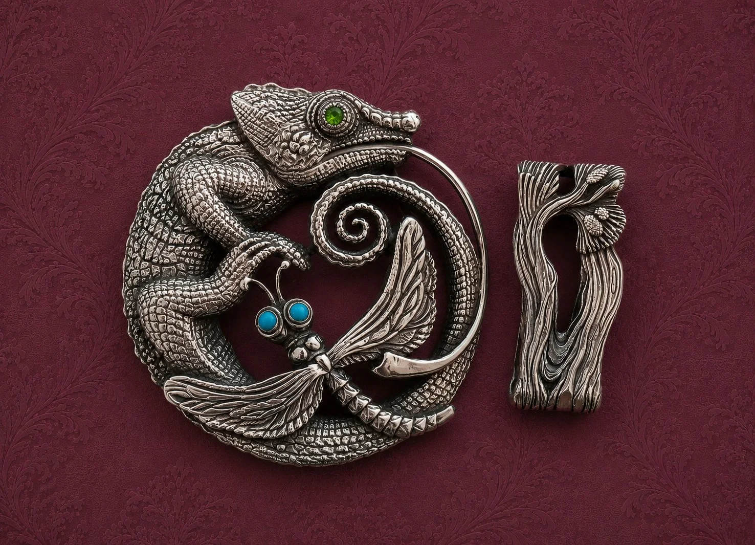 Close-up of silver jewelry shaped like a chameleon, butterfly, and a tree trunk, displayed on a dark red textured background.