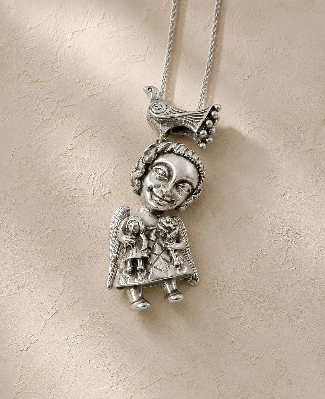Silver necklace with a pendant of a smiling angel girl with wings, holding two smaller angel dolls, and a bird sitting on top.