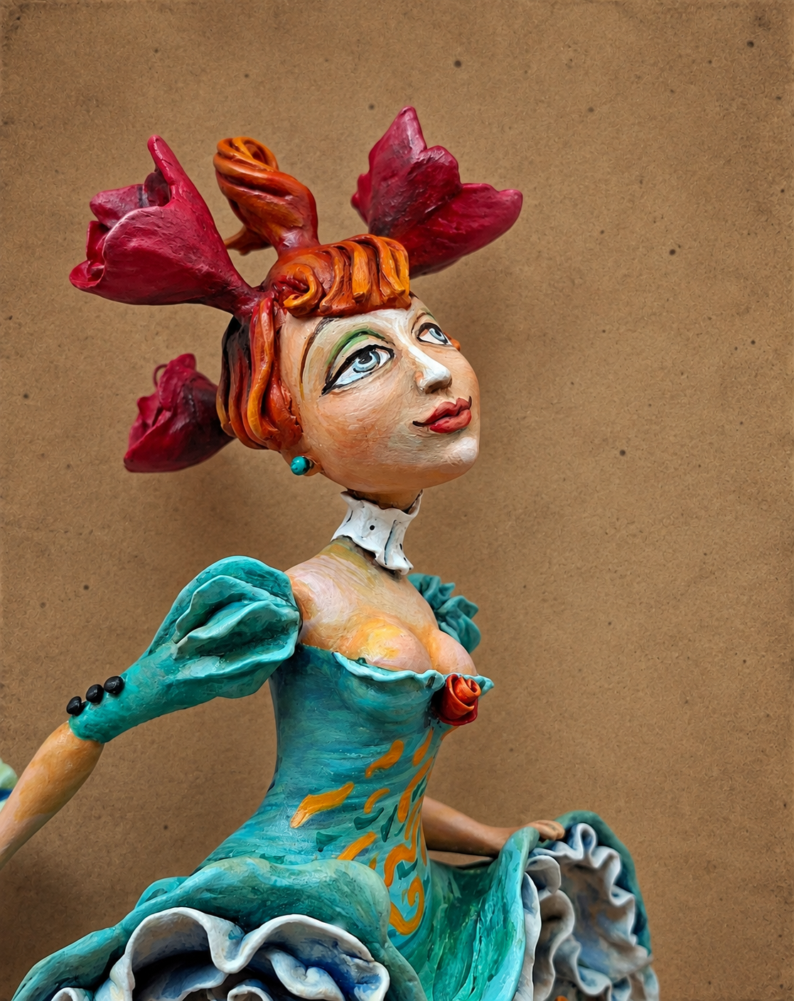 Colorful ceramic sculpture of a woman with red flower-shaped hair, wearing a turquoise dress with orange and yellow patterns, against a plain brown background.