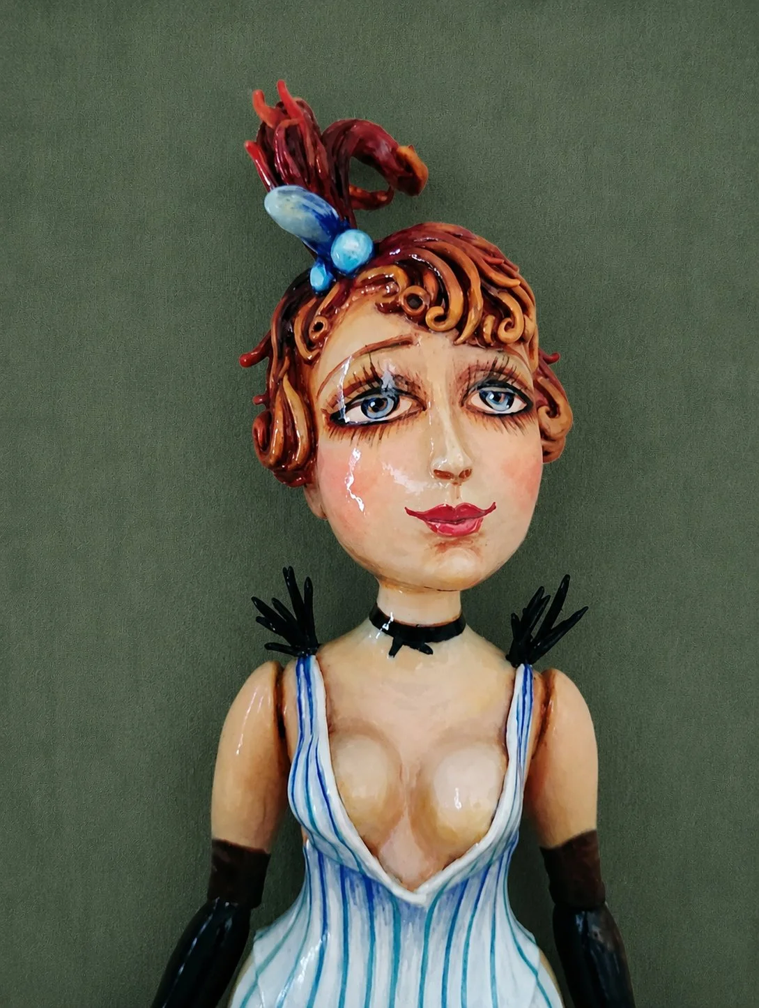 A female figurine with blue eyes, red hair styled with a blue decorative accessory, wearing a blue and white striped dress, a black choker, and black gloves.