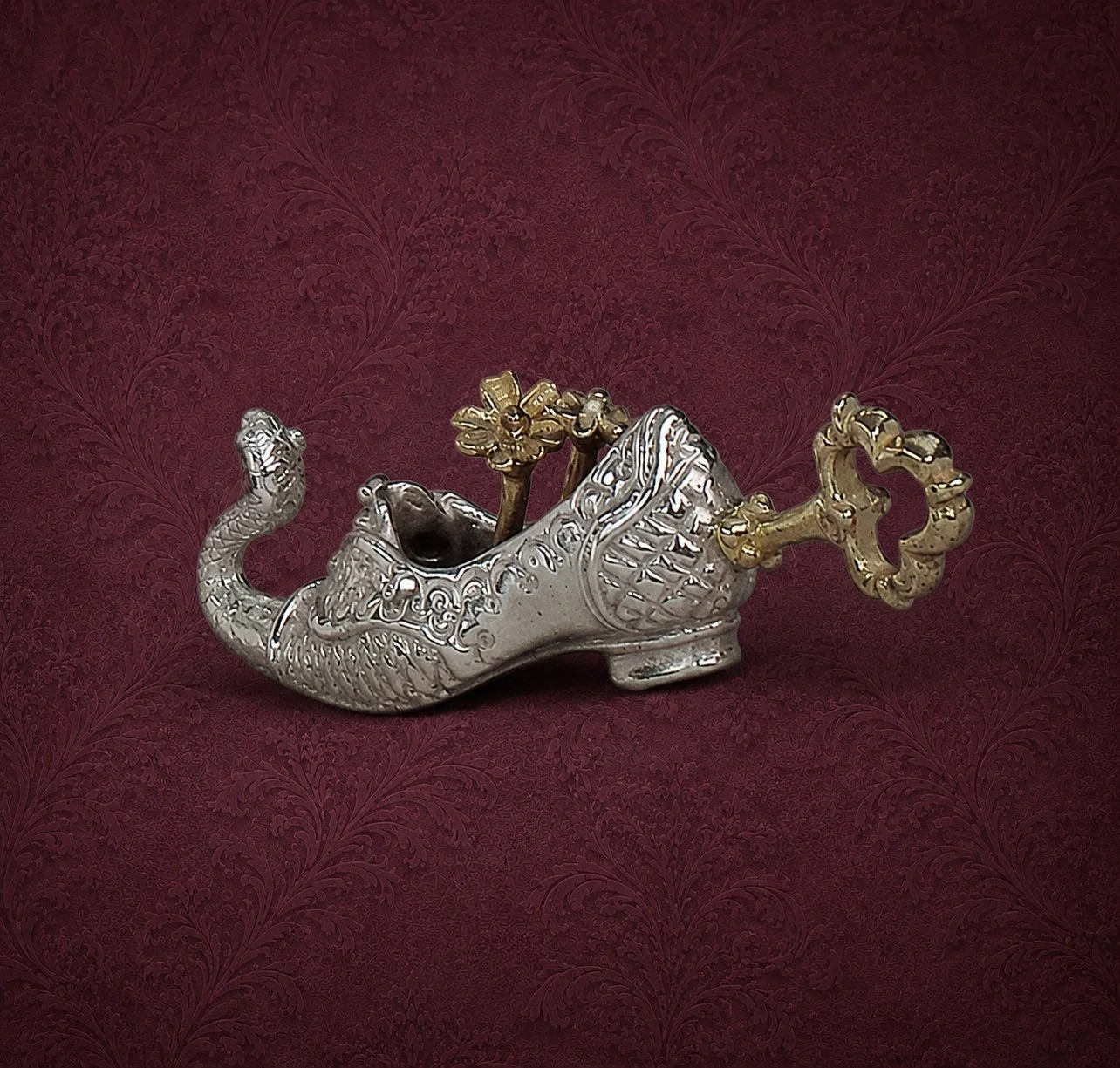 A decorative silver boat-shaped jewelry container with a dragon head on the front and golden floral handle and ornament, set against a red textured background.