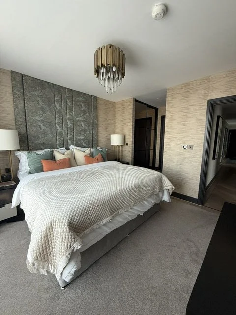 Modern hotel bedroom with a king-sized bed, decorative pillows, two bedside lamps, a chandelier, and textured wall panels.