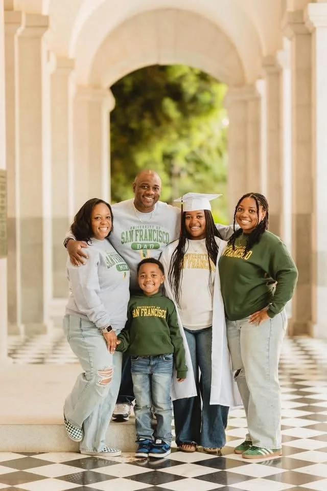 Family celebrating graduation indoors at a university, with a graduate in a cap and gown in the center. malonn barnes Daughter annocing going to the University of San Francisco in the Fall 26