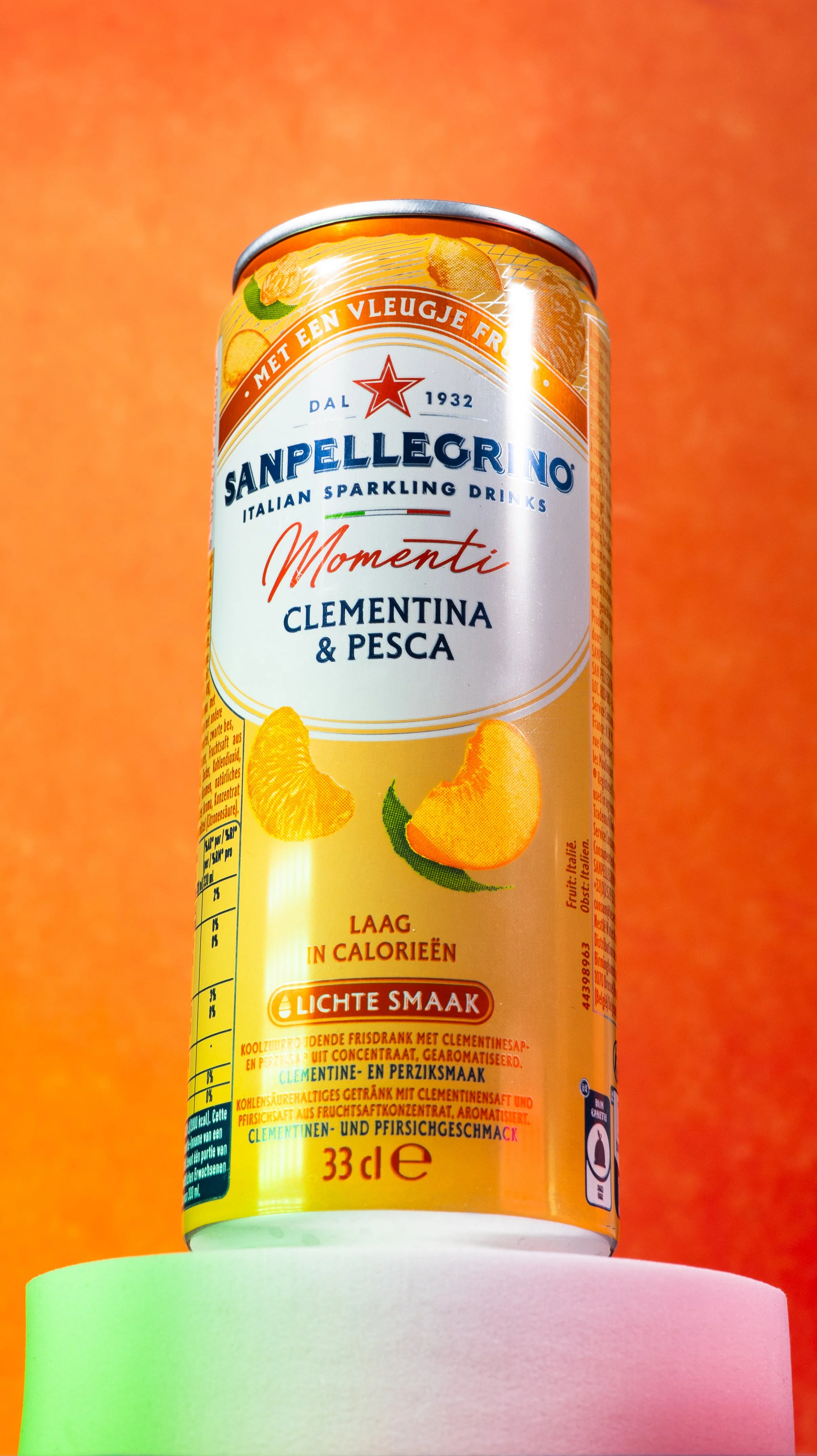Une canette de boisson gazeuse italienne Sanpellegrino goût clémentine et pêche sur un fond orange, vue partiellement.