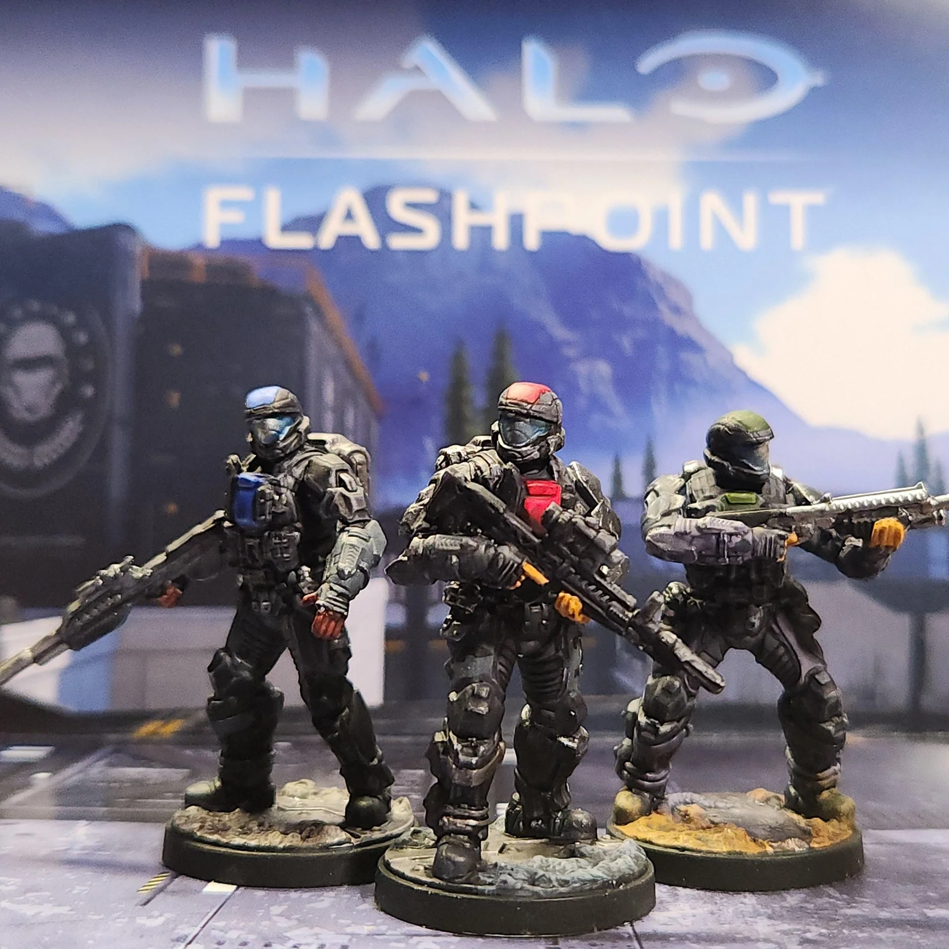 Set of six miniature military action figures in combat gear, standing on rocky bases, with a backdrop featuring a mountain range and a sign reading "HALO FLASH-POINT".