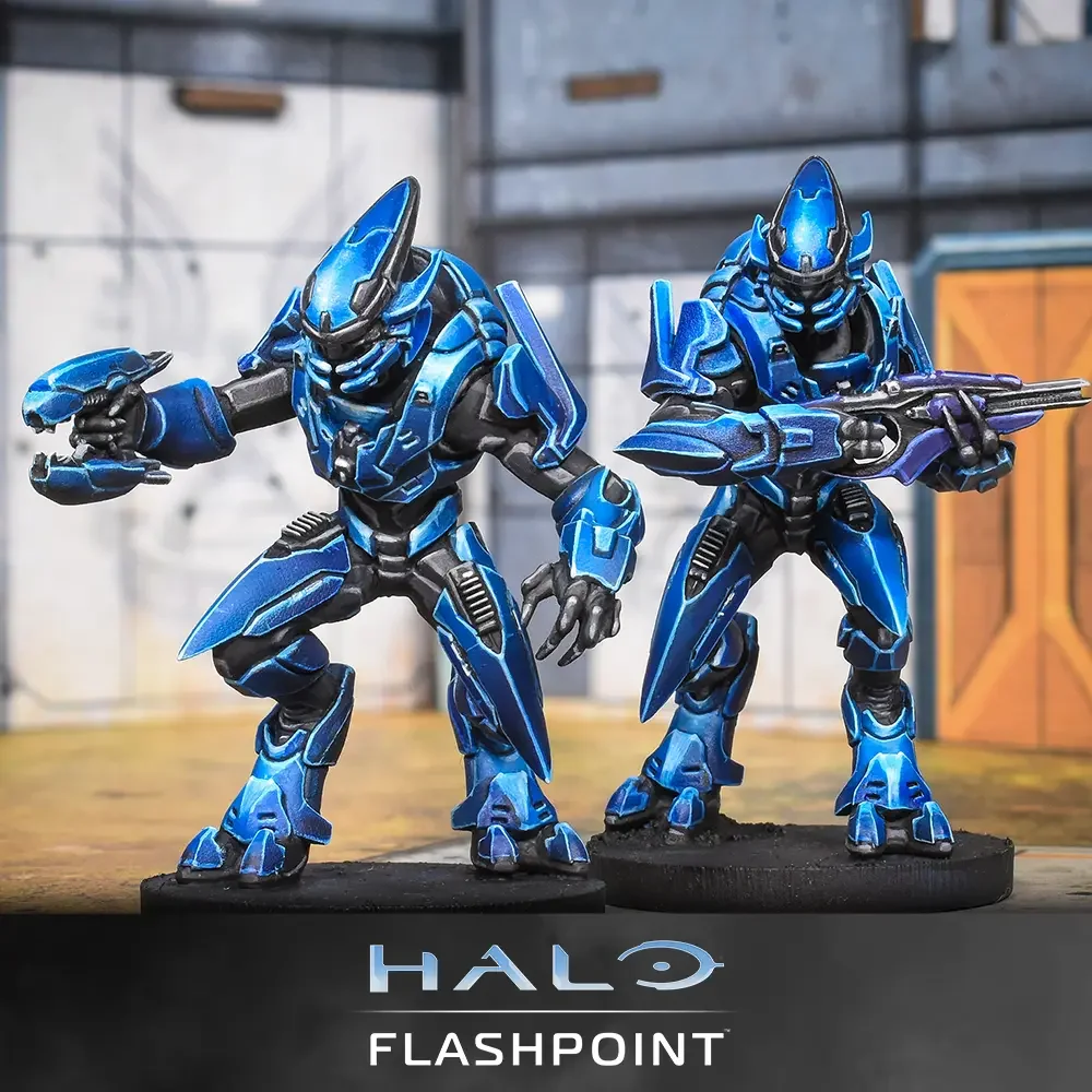 Two blue and black Halo characters figurines standing on a table, with a backdrop resembling a sci-fi setting, and the text 'Halo Flashpoint' at the bottom.