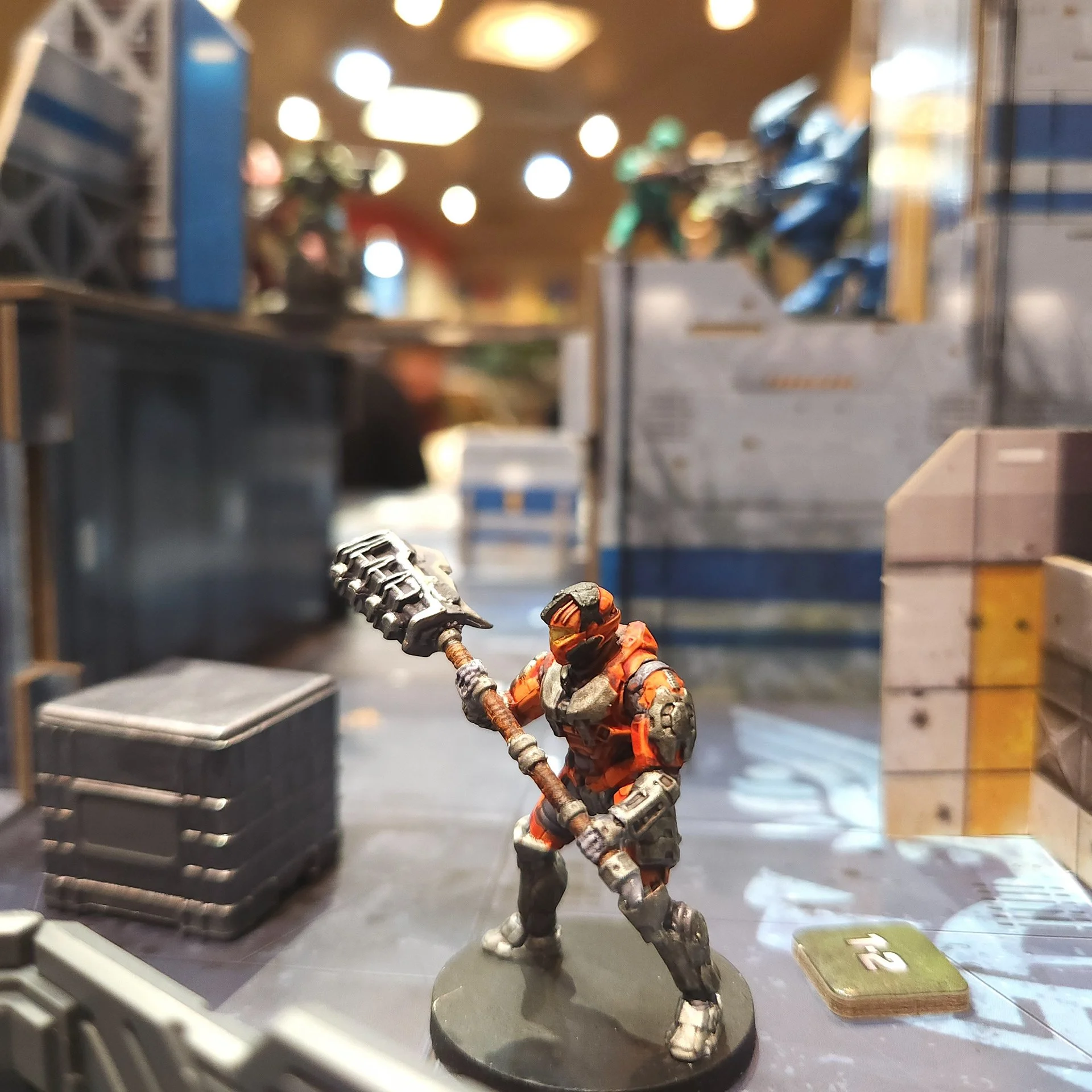 Miniature action figure of a soldier wearing an orange and gray uniform, holding a staff, standing on a black base in a store environment.