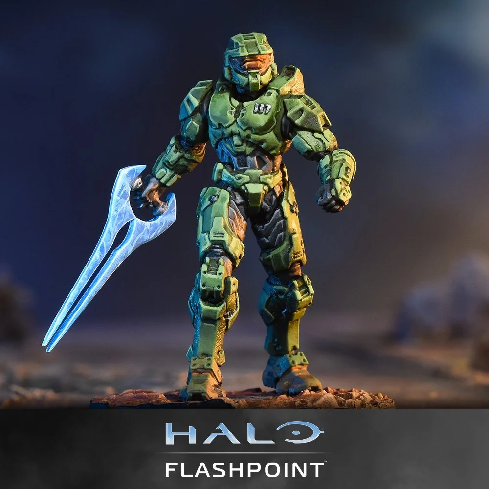 A detailed action figure of a green armored soldier from Halo, holding a glowing futuristic weapon, standing on a rocky surface with a dark, cloudy background. The bottom has the Halo FlashPoint logo.