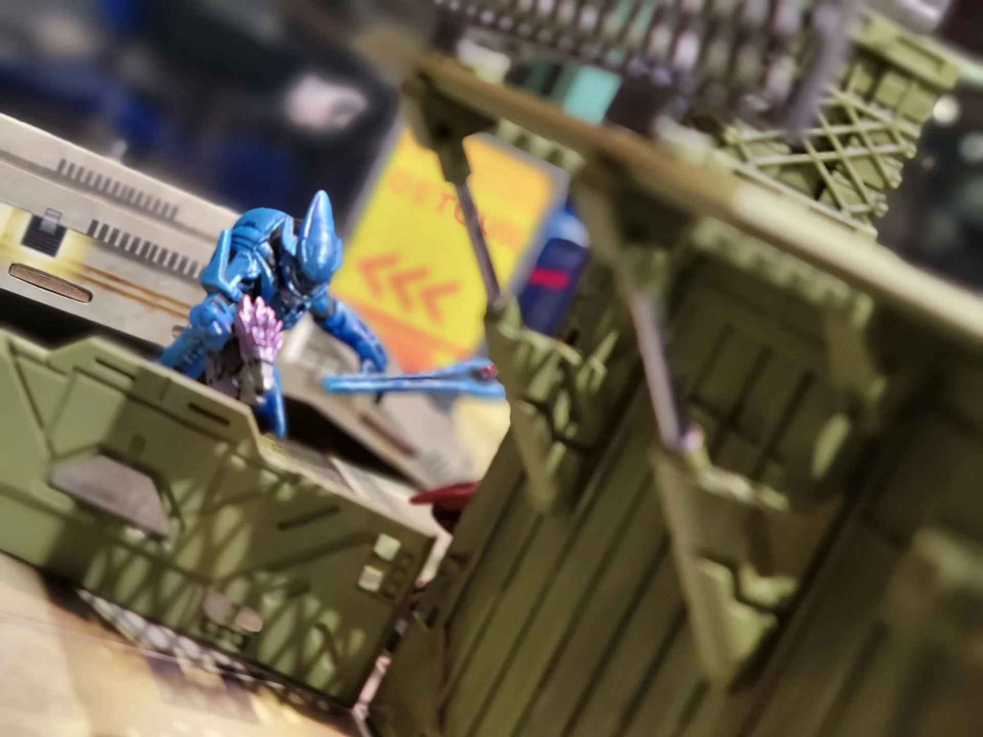 Close-up of a blue toy dinosaur inside a green plastic storage bin with a yellow and red object in the background.