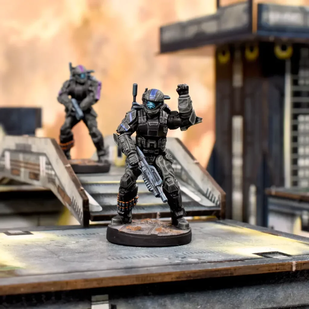 Two miniatures of soldiers in tactical gear, one in foreground raising a fist and holding a gun, the other in background on stairs, with a futuristic city setting.
