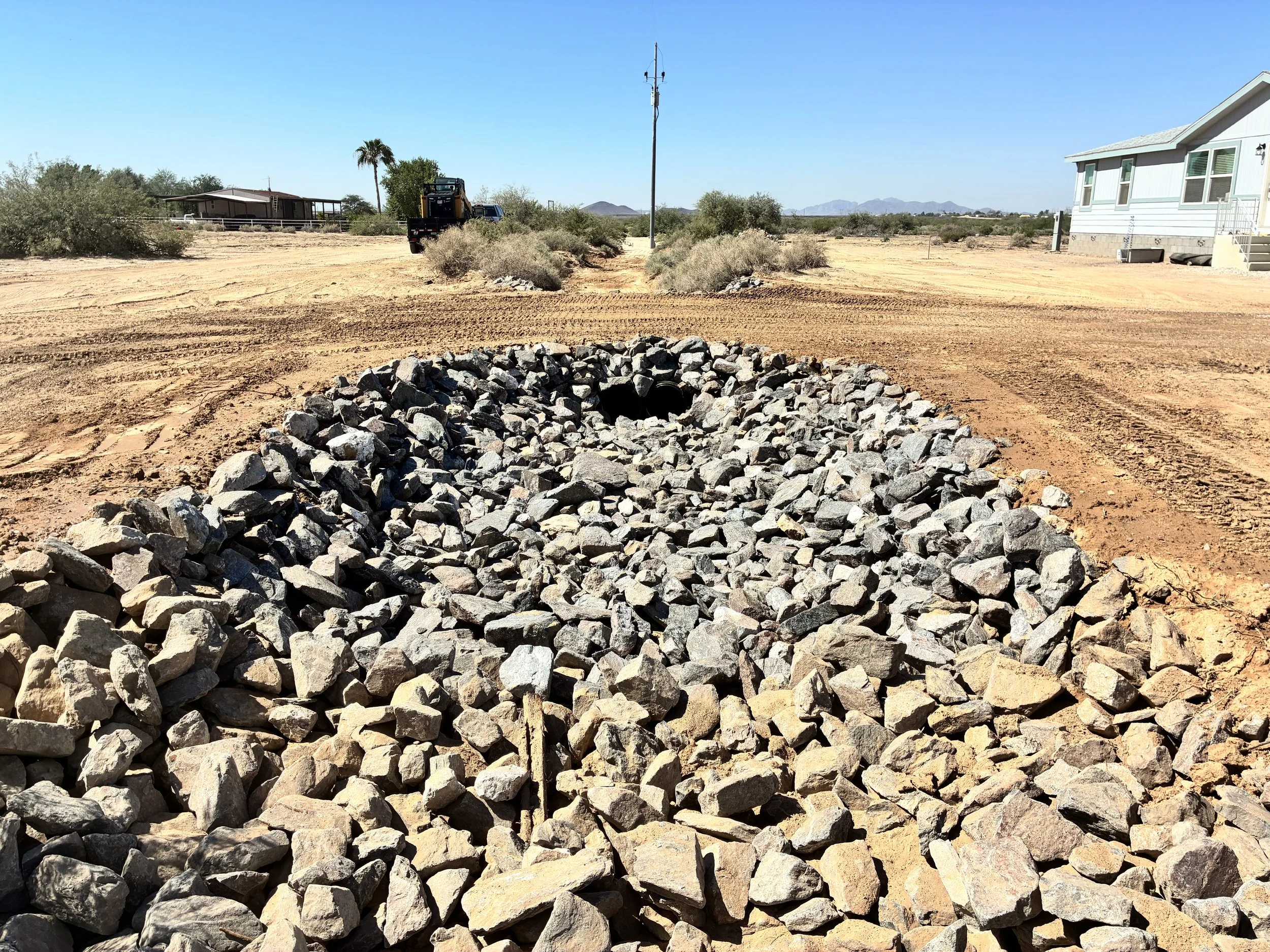 Completed riprap apron around twin culvert openings beneath a driveway crossing.