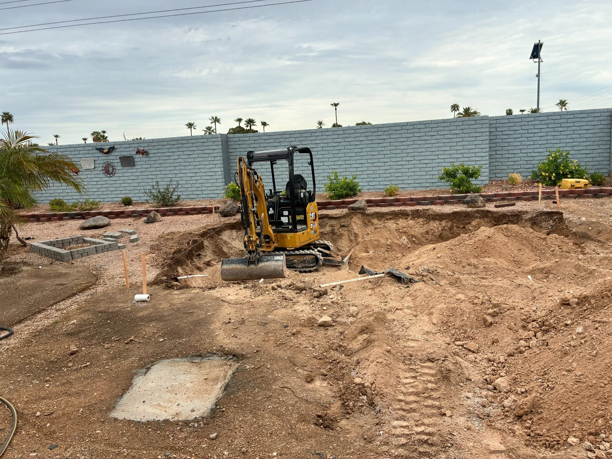 Compact excavator completing a backyard pool dig with layout lines and grade control