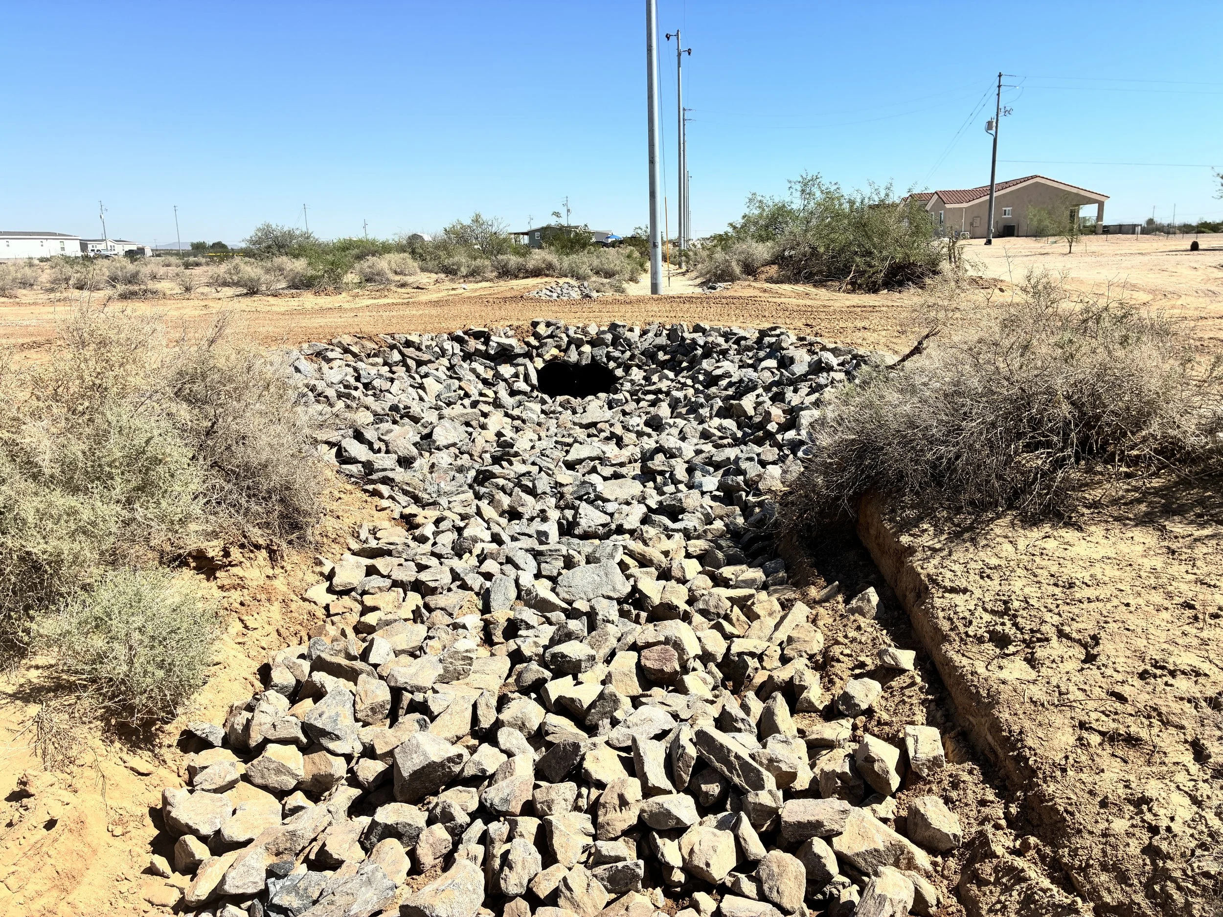 Rock-lined drainage channel leading to the culvert at the finished driveway crossing.
