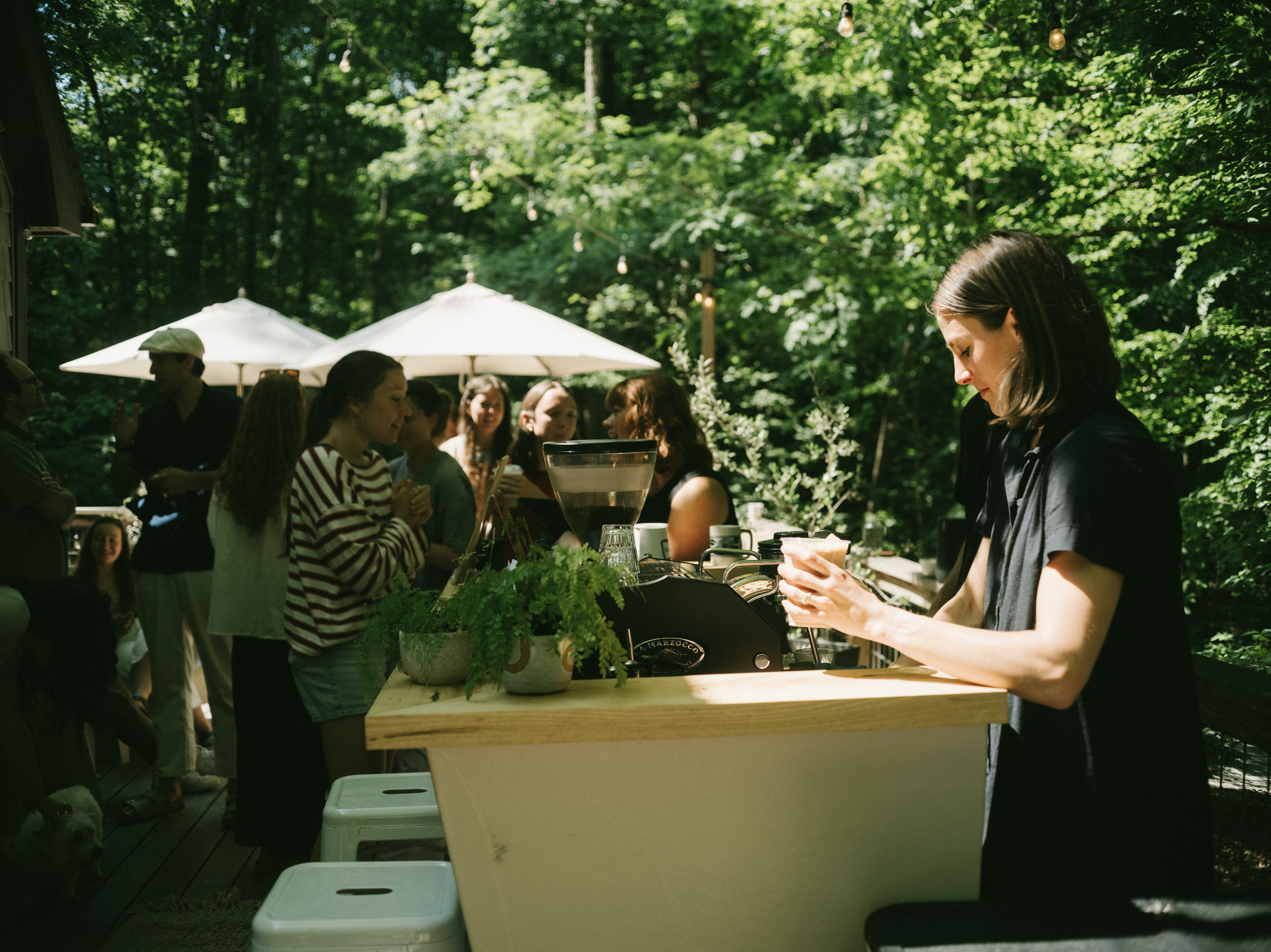 A group of people gathered outdoors around a custom espresso bar enjoying their custom coffee catering experience.