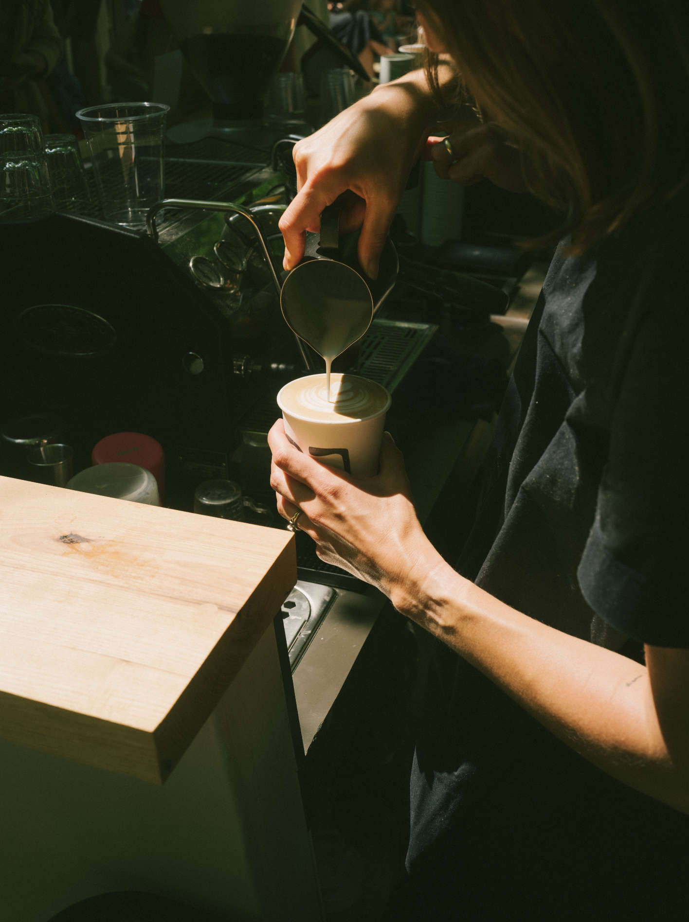 Barista pouring steamed milk into a cup of coffee to create latte art in a coffee shop.