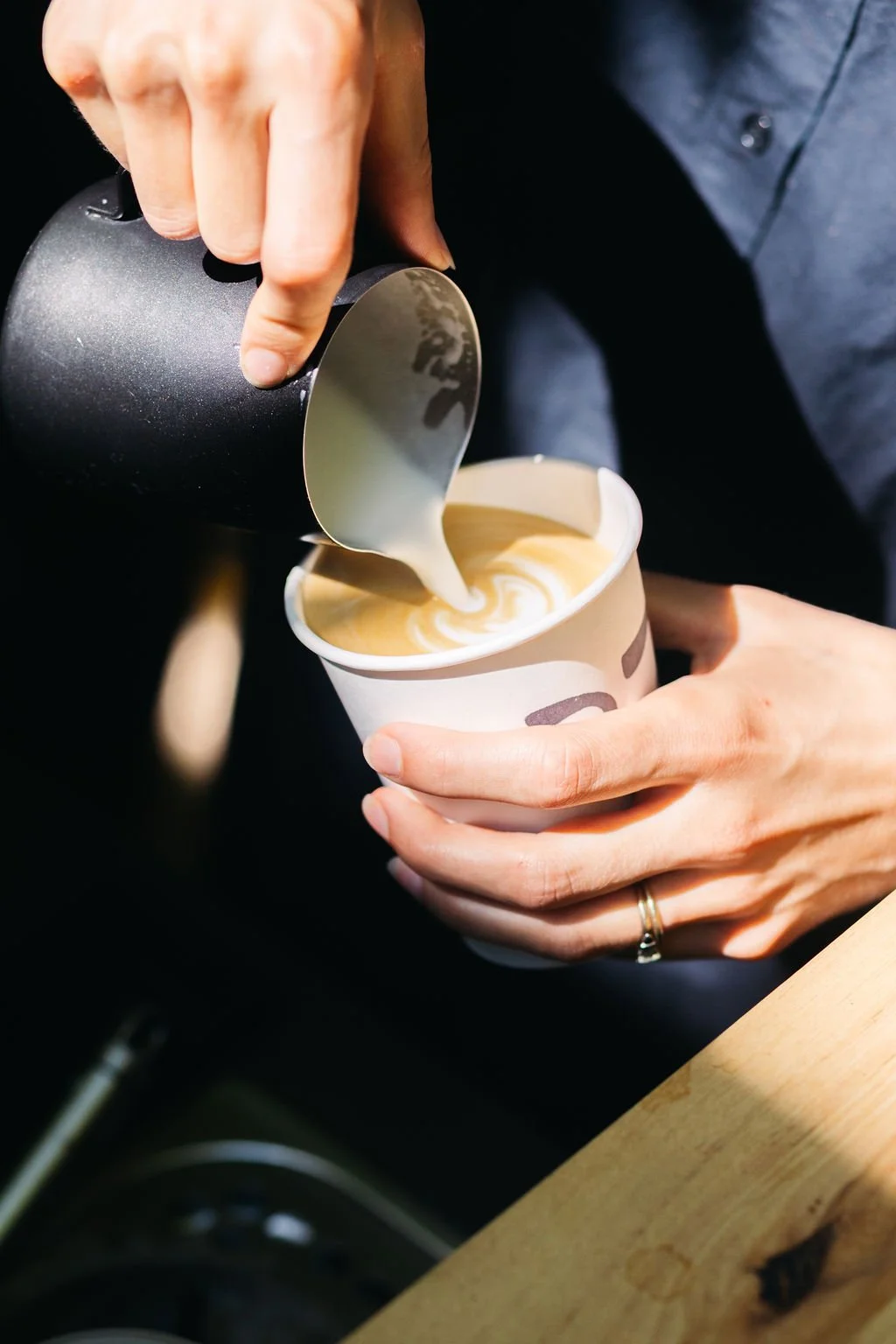 Person pours steamed milk into a cup of espresso to make a latte, with a swirl pattern visible on top.