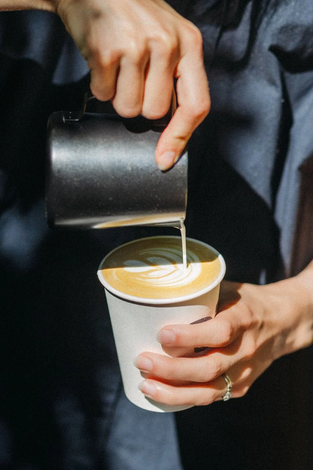 A person is pouring cream into a cup of coffee to create latte art.