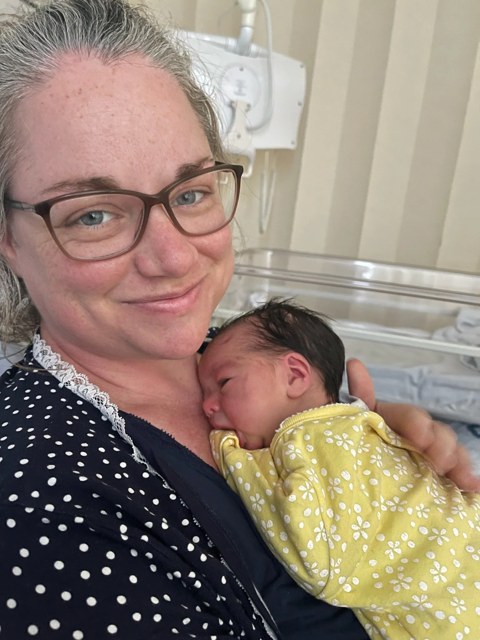 woman in hospital smiling at the camera with a baby on her chest