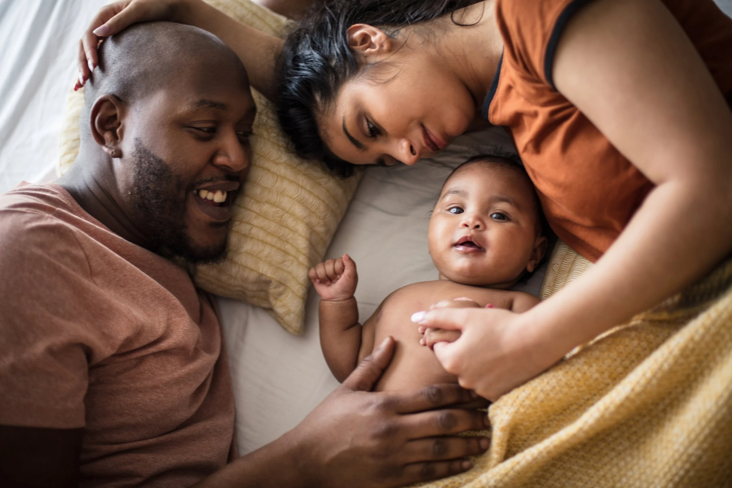 Happy family including mum, dad and baby lying in bed looking at their baby
