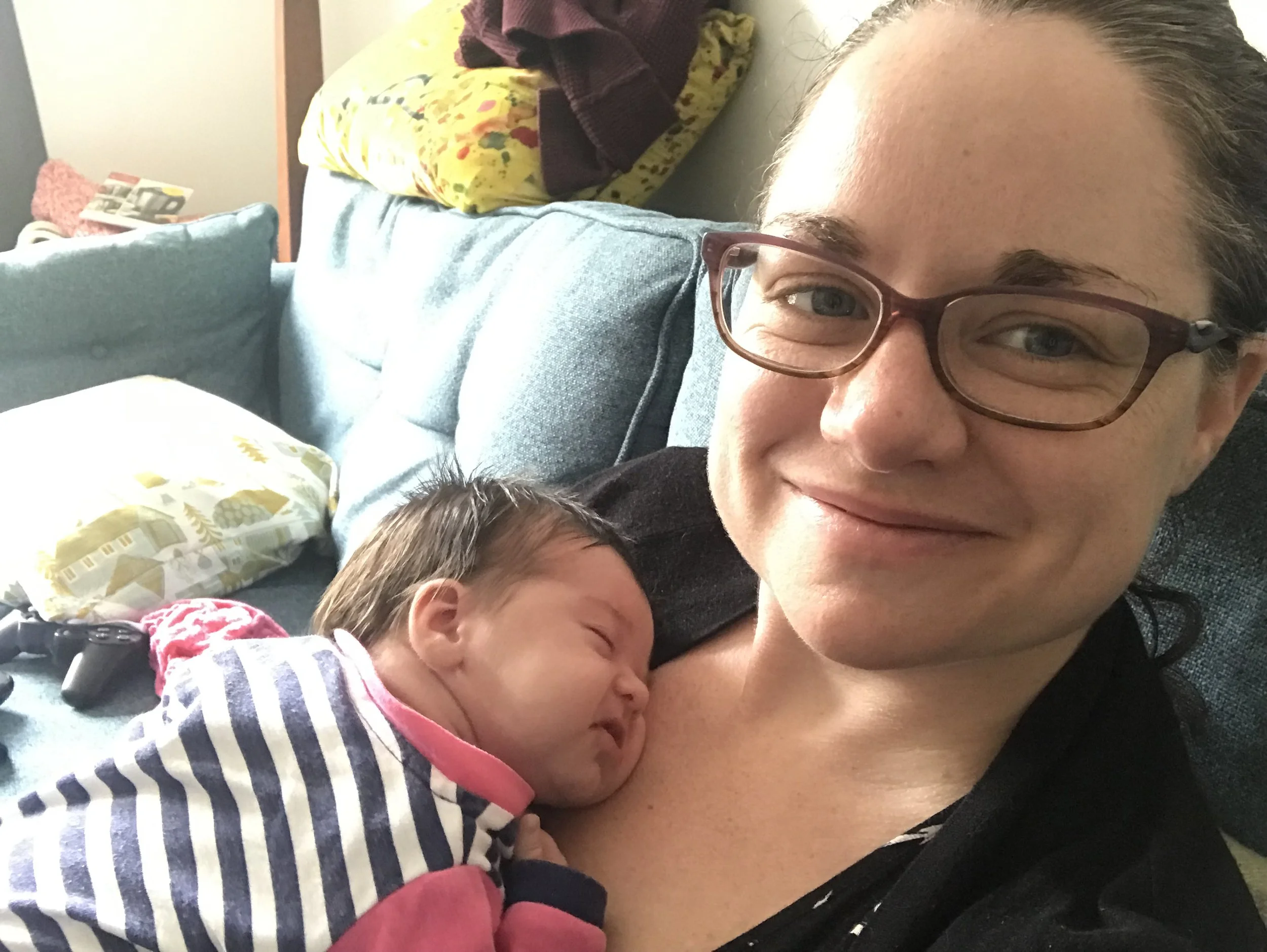 woman smiling at the camera with a baby asleep on her chest
