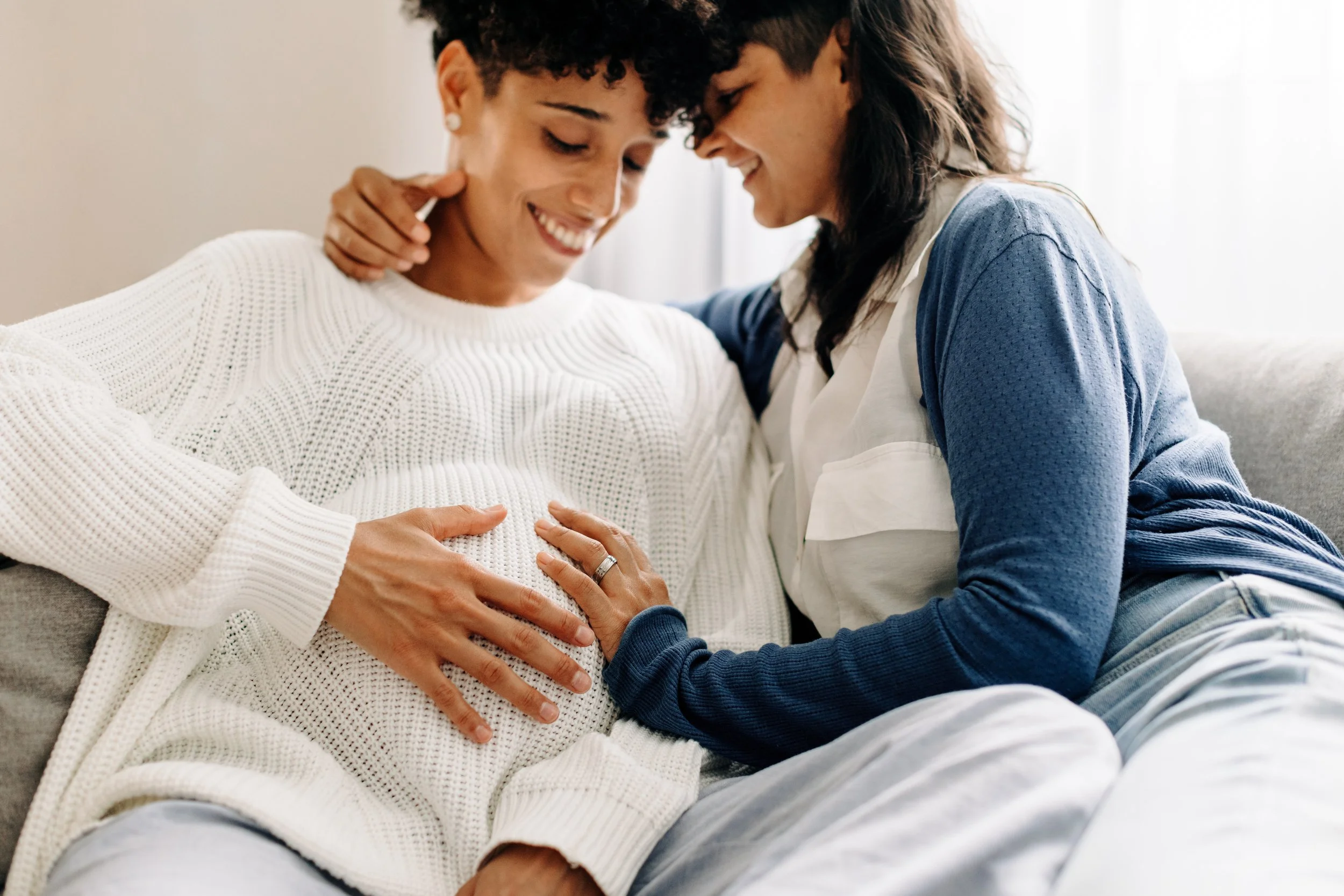 A pregnant gay couple embracing each other with their hands on the pregnant woman's bump
