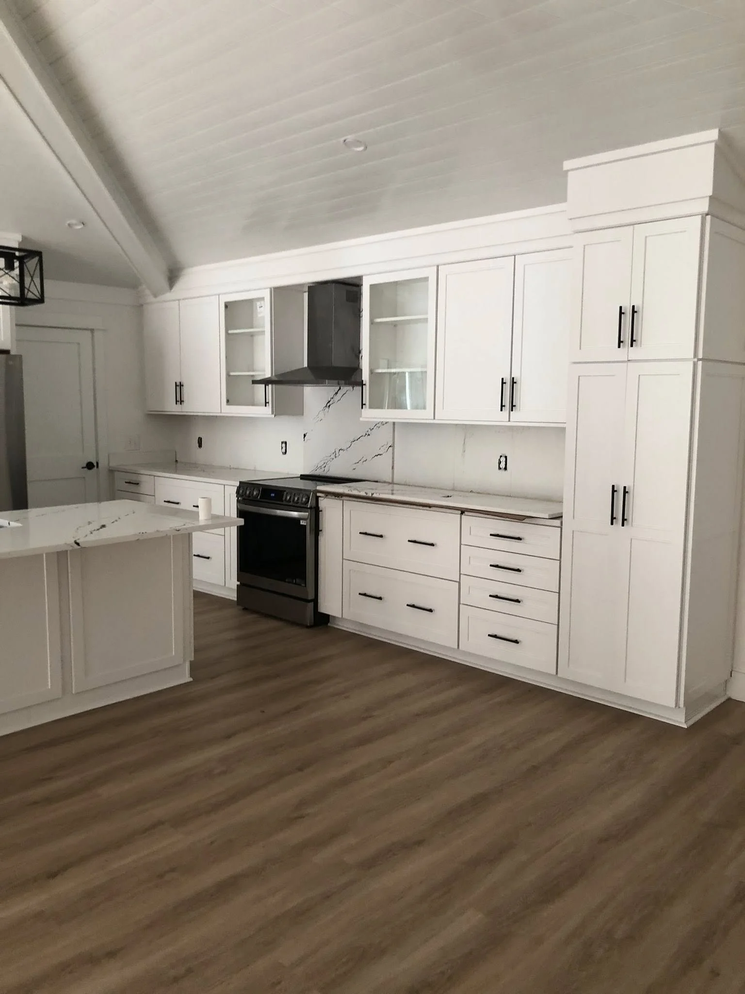 A kitchen with white cabinets, a marble countertop, stainless steel stove, and wood flooring.