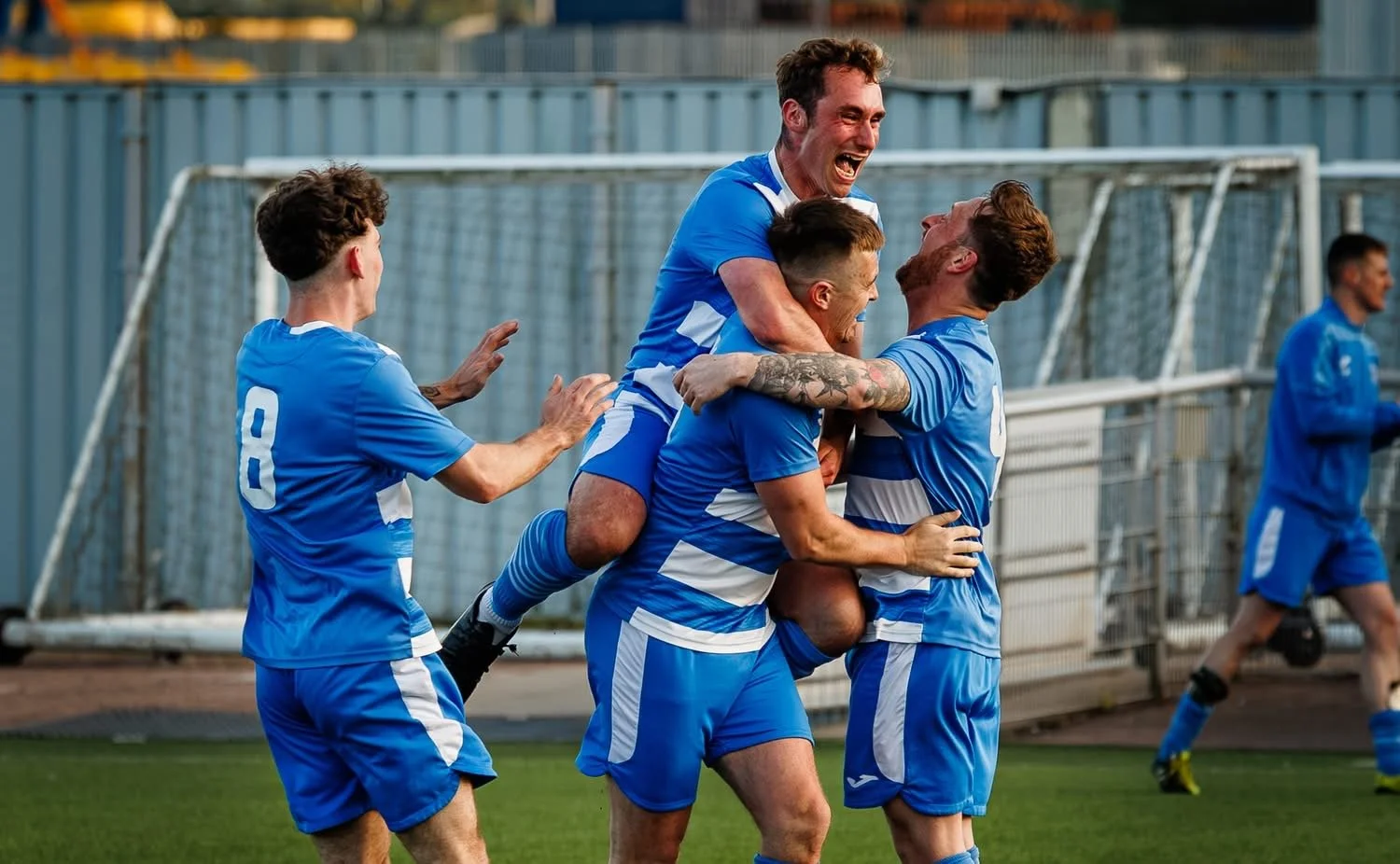 Soccer players in blue uniforms celebrating a goal together on the field.