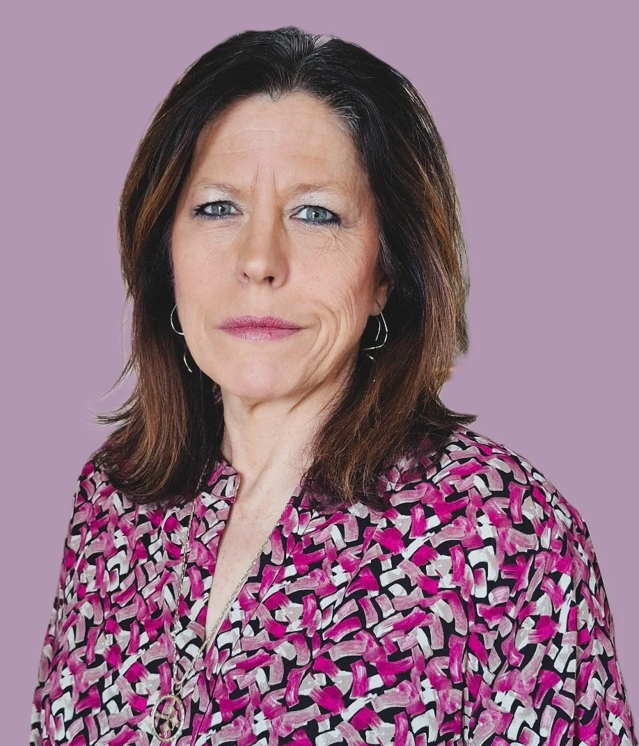 Faith Wolfley with shoulder-length brown hair, blue eyes, and light skin, wearing a pink, black, and white patterned blouse, standing against a purple background.