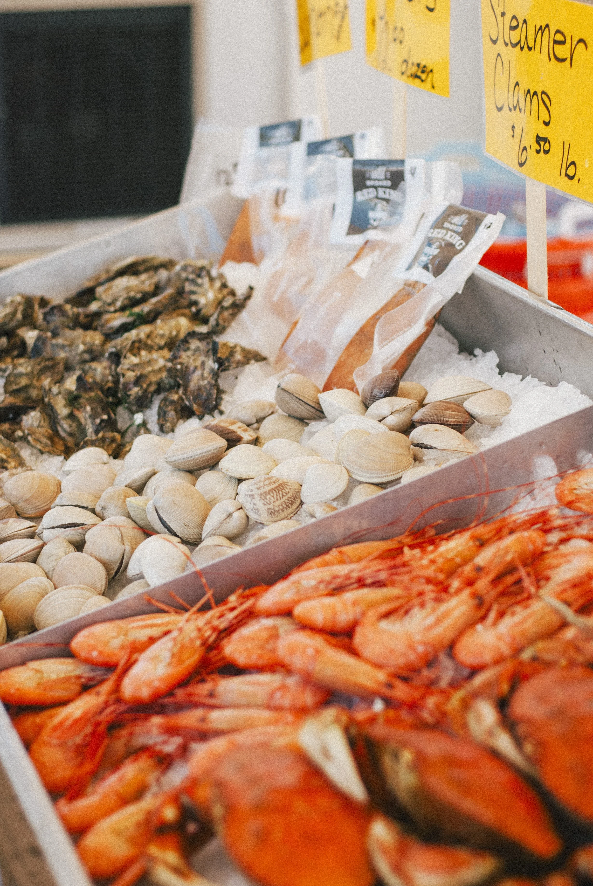 Seafood display with clams, shrimp, and other shellfish on a bed of ice at a market.
